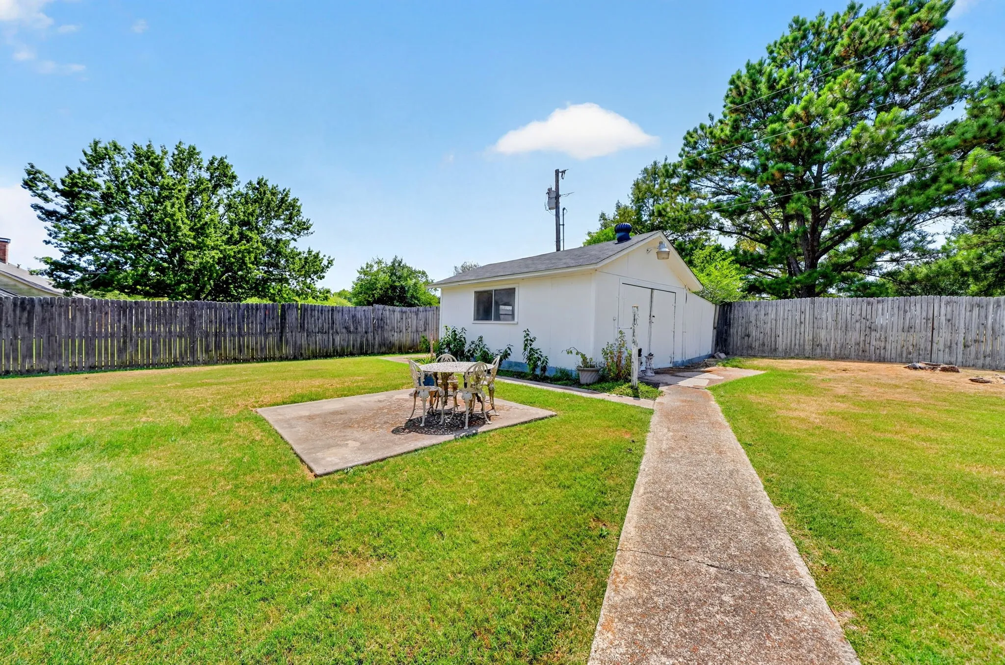 Expansive lawn area with a concrete patio, perimeter wood fencing, and a detached white-sided shed