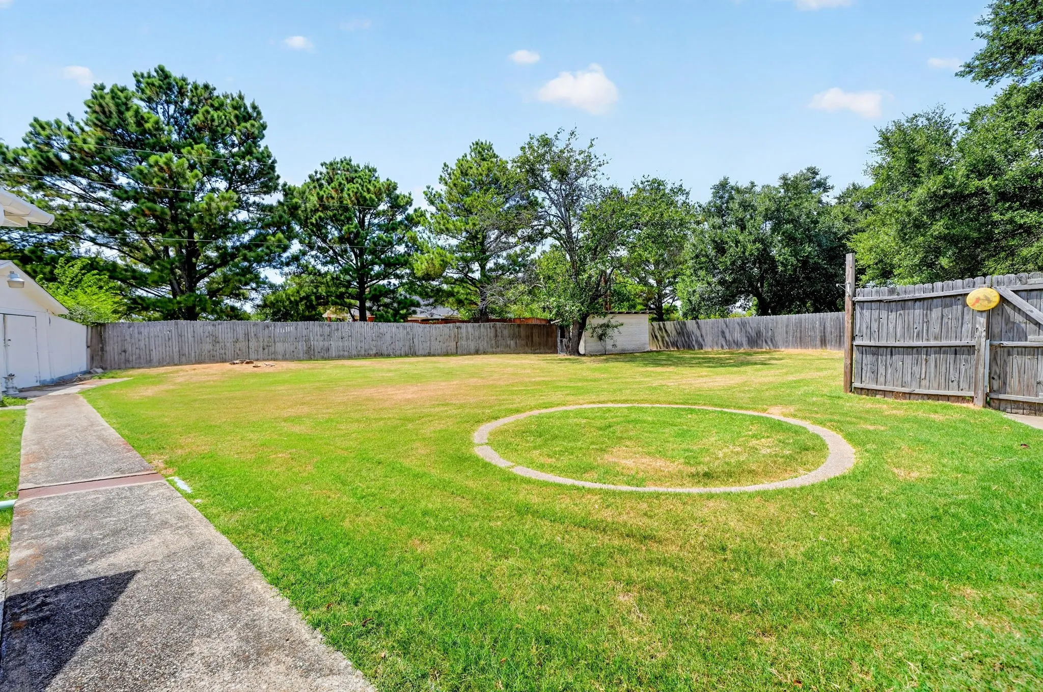 Expansive grassy backyard featuring a perimeter fence and concrete pathway