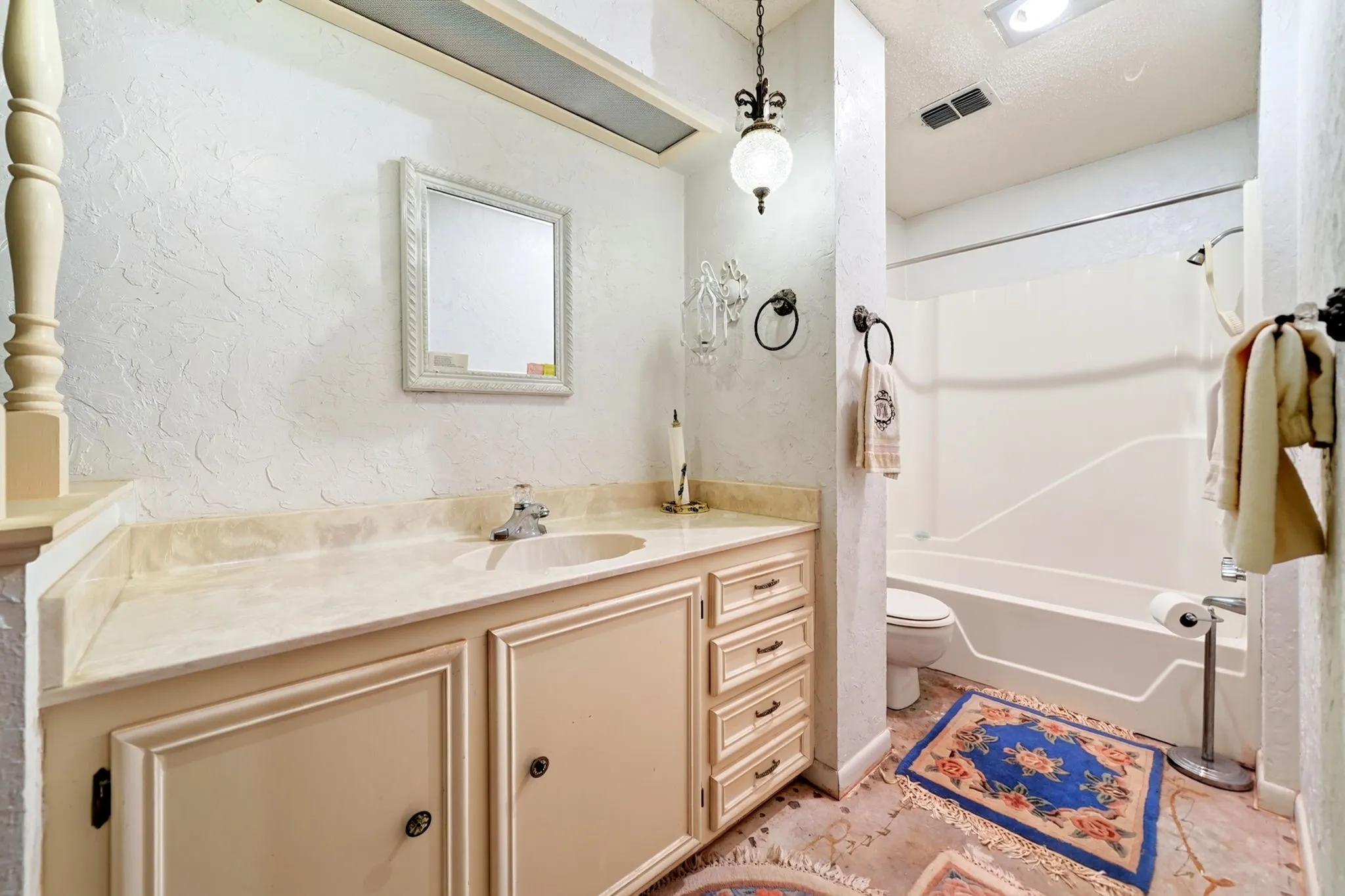 Vanity with integrated sink and chrome faucet, custom cabinetry with ornate drawer pulls, wall-mounted mirror, and overhead pendant light fixture