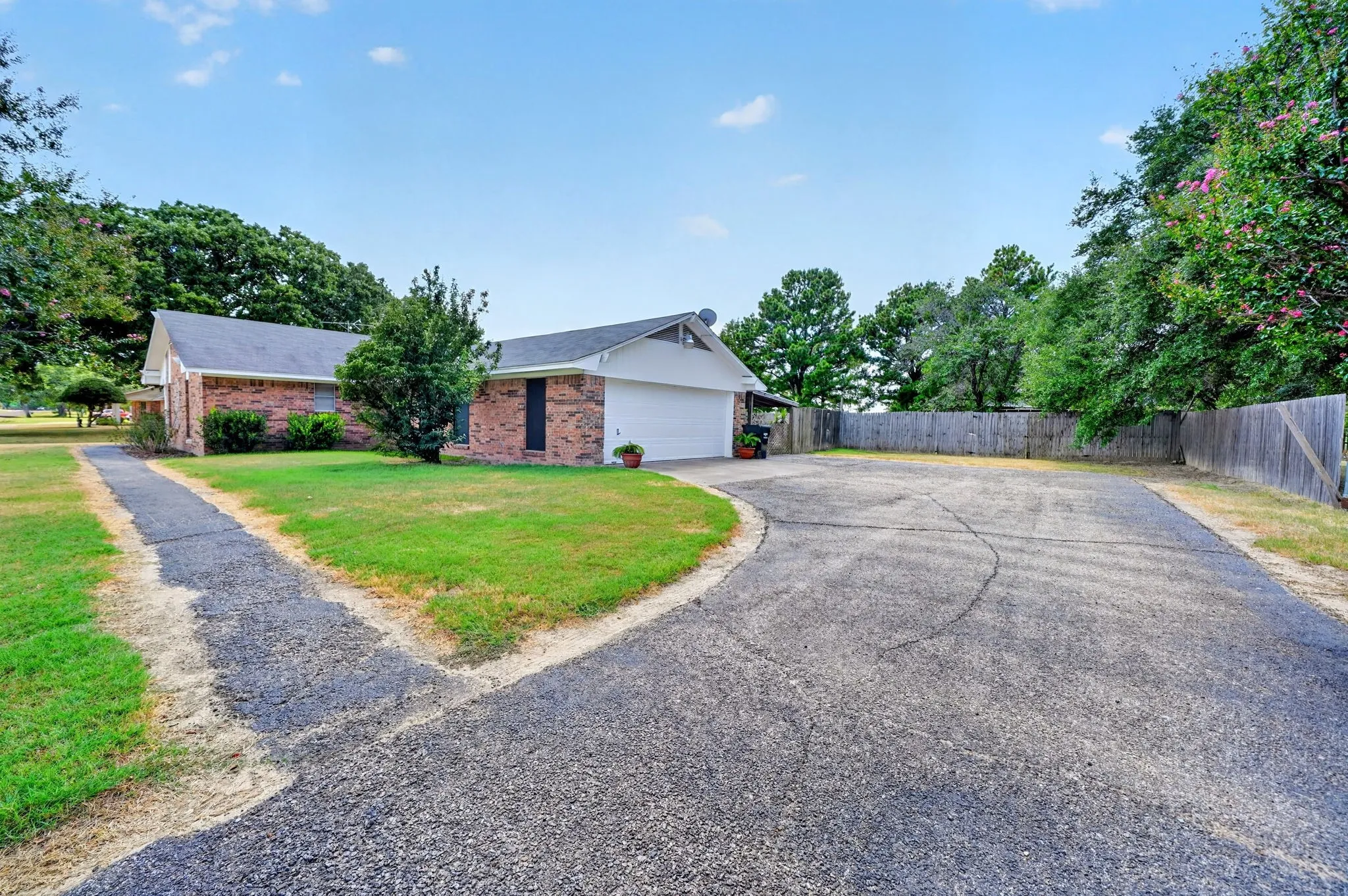 Brick exterior residence with an attached garage, featuring a paved driveway and a wooden privacy fence
