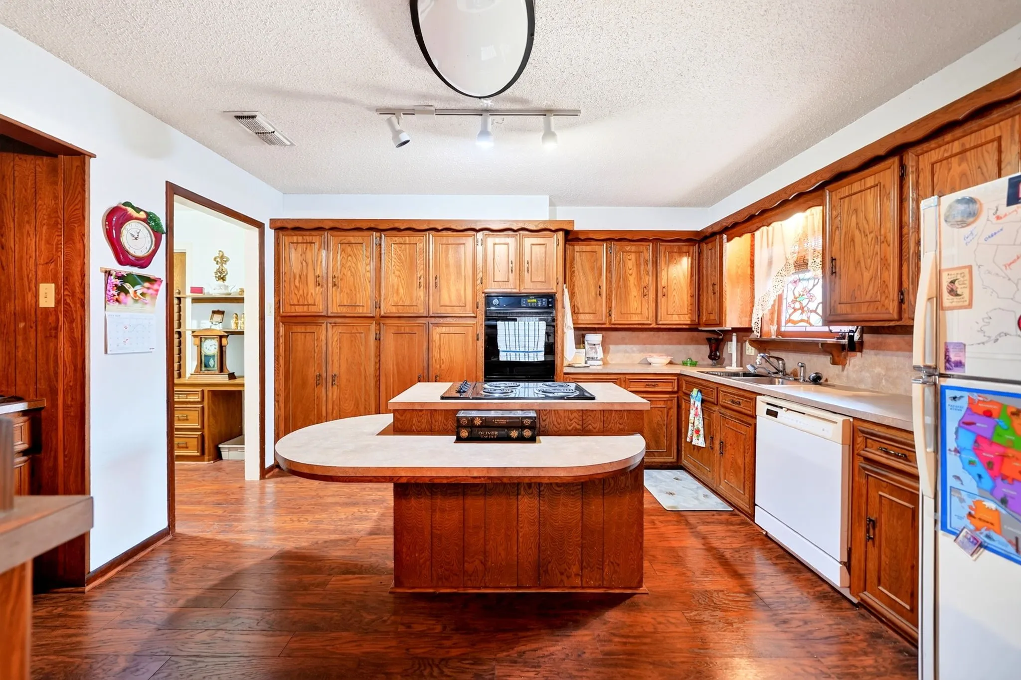 Kitchen featuring wood-finish flooring, wood cabinetry, built-in oven, and a center island with a cooktop