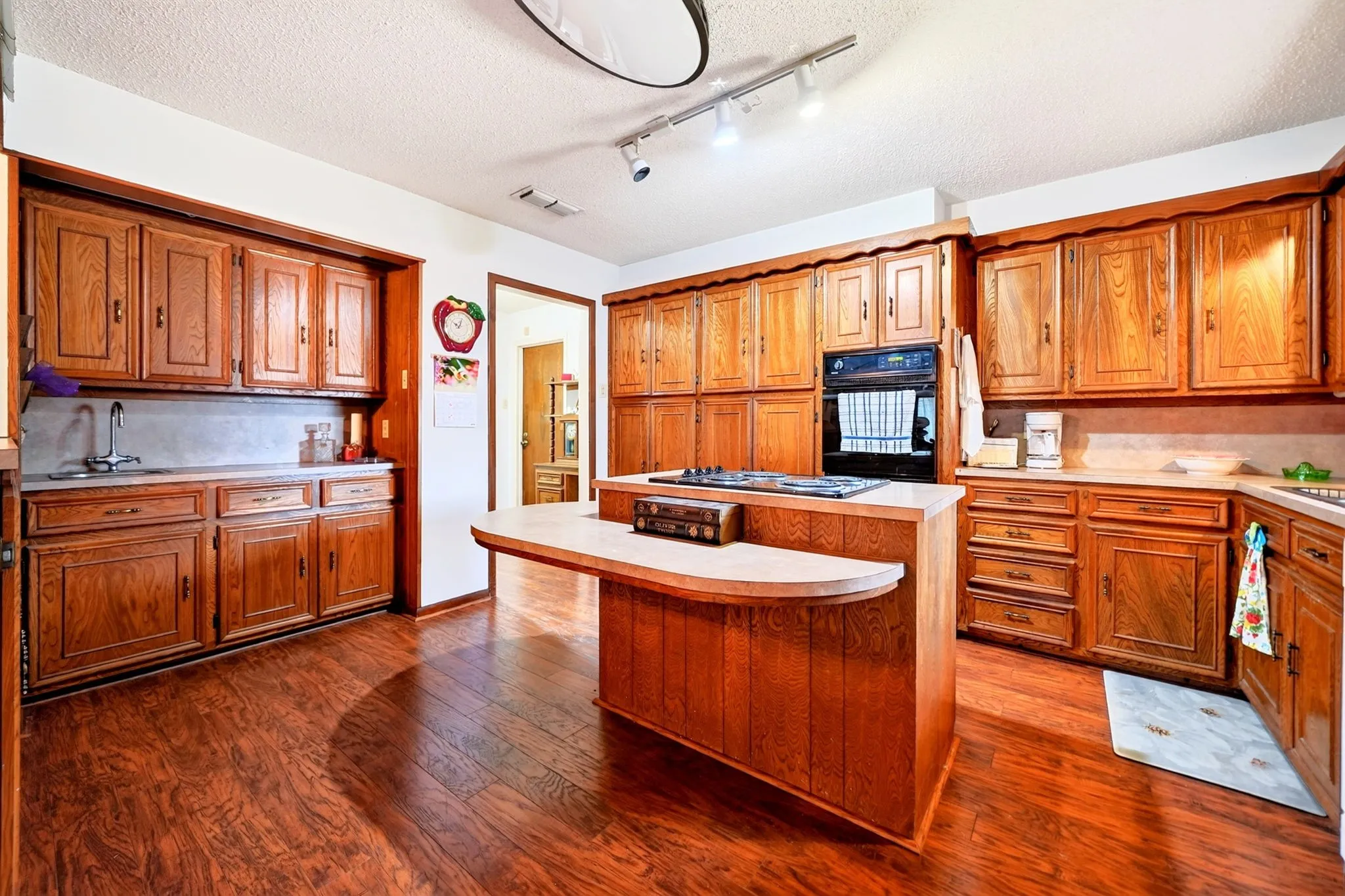 Wood-finish flooring throughout, extensive cabinetry with wood finishes, built-in oven, and a kitchen island with integrated cooktop