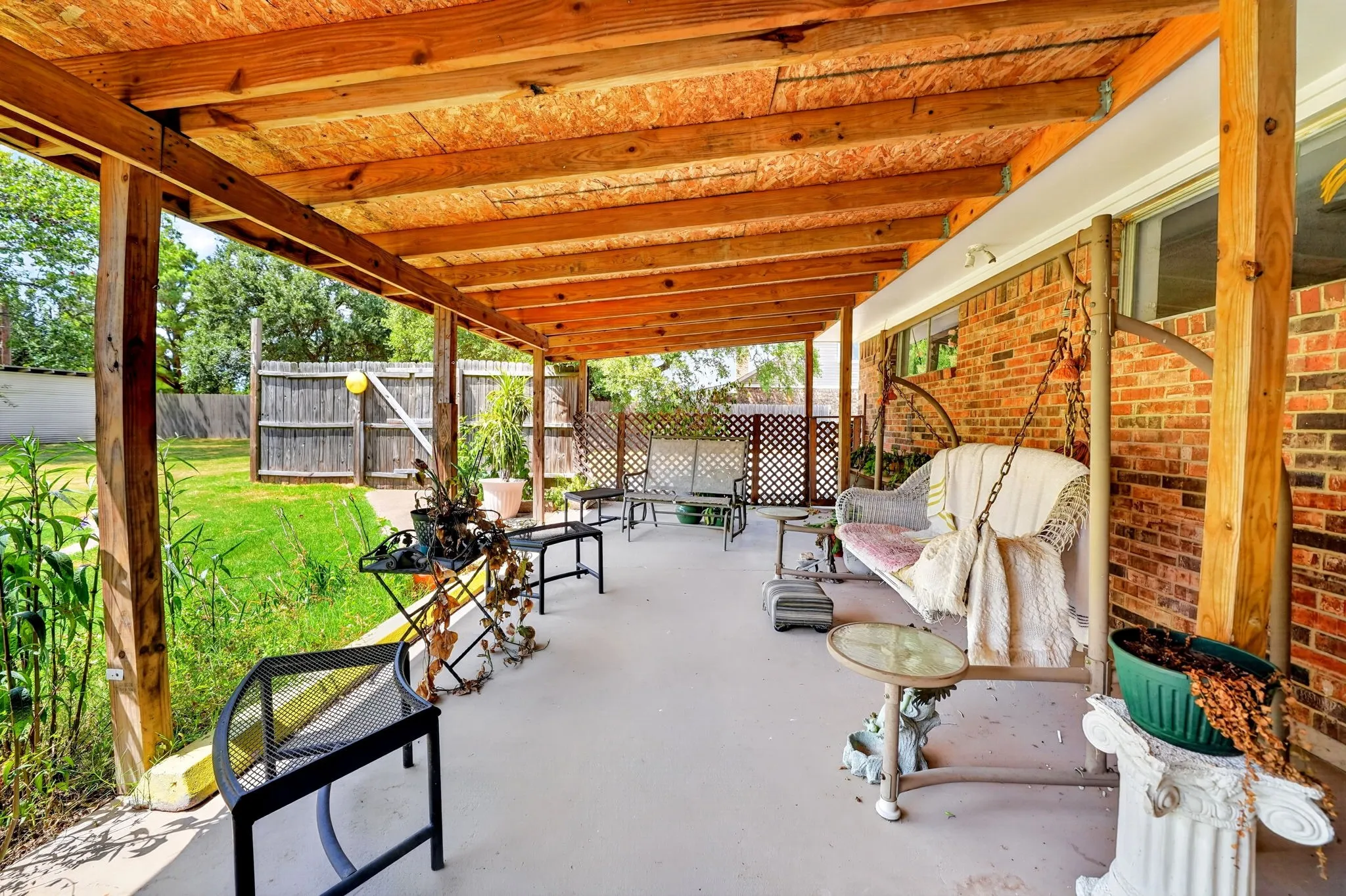 Covered patio with a wood-beam ceiling, concrete flooring, and brick exterior wall