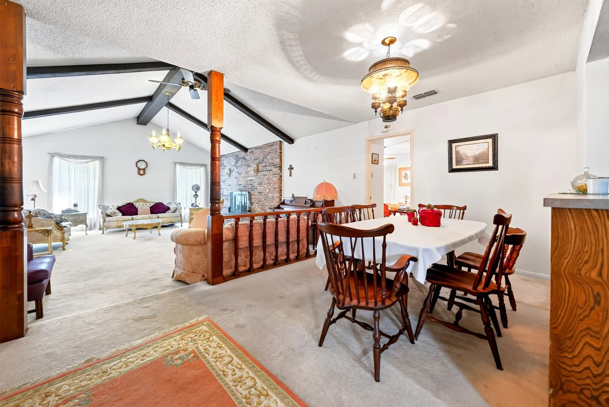 Vaulted ceiling with exposed beams, stone accent wall, wood-finish columns, and a built-in wood-finish breakfast bar