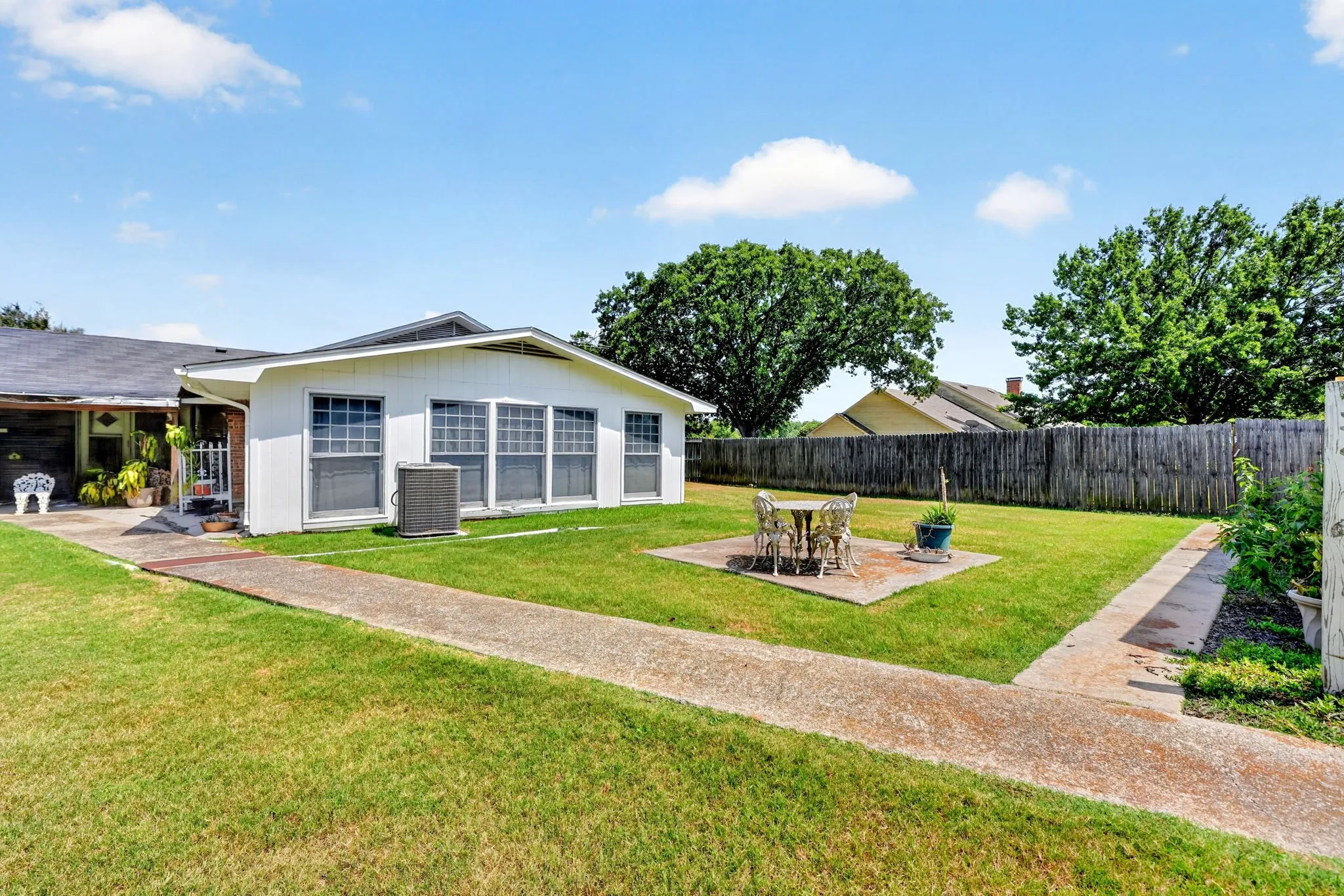 Spacious rear yard with a concrete patio, fenced perimeter, and mature trees