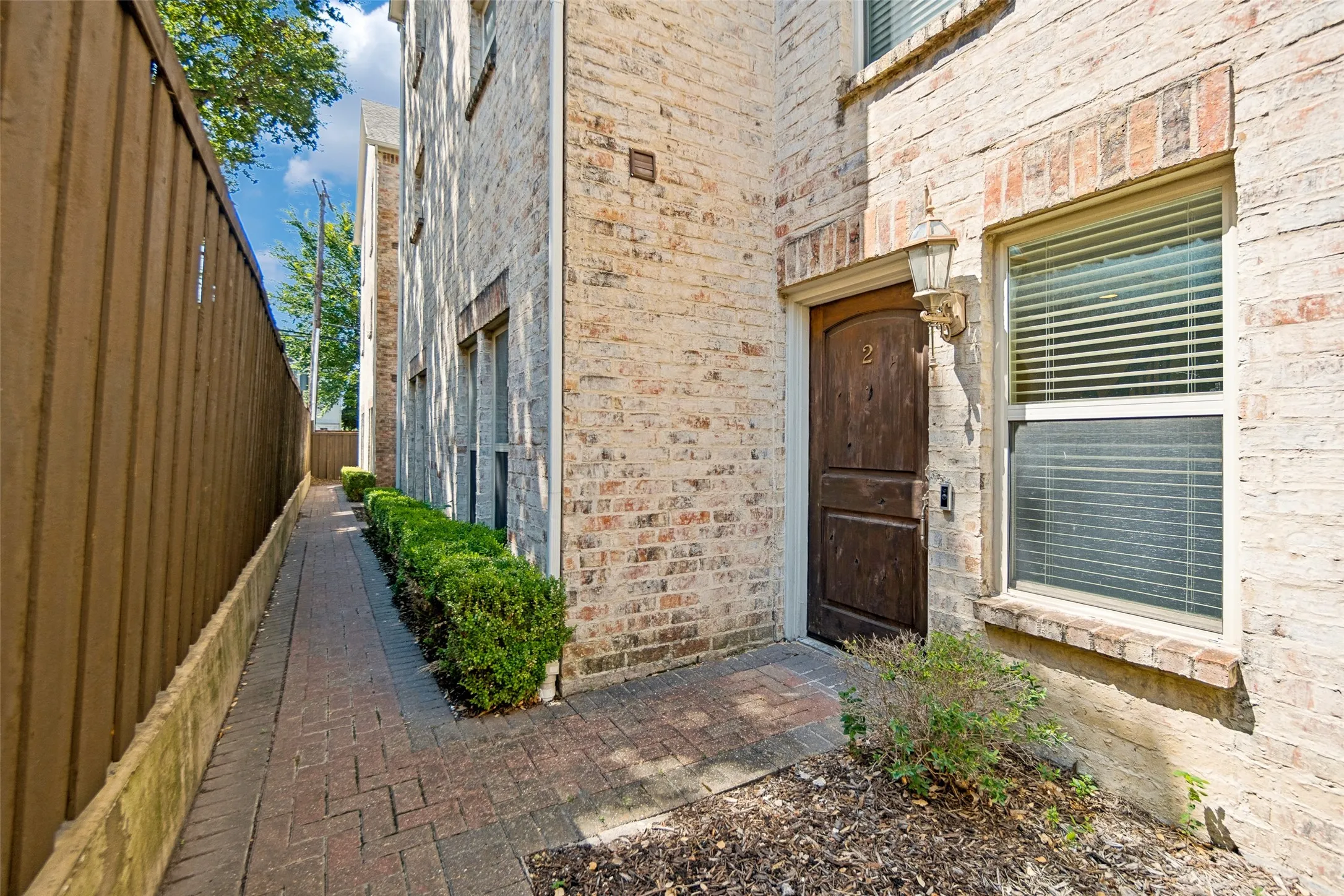 Brick exterior with a dark wood-finish entry door, decorative outdoor sconce, and a paver walkway