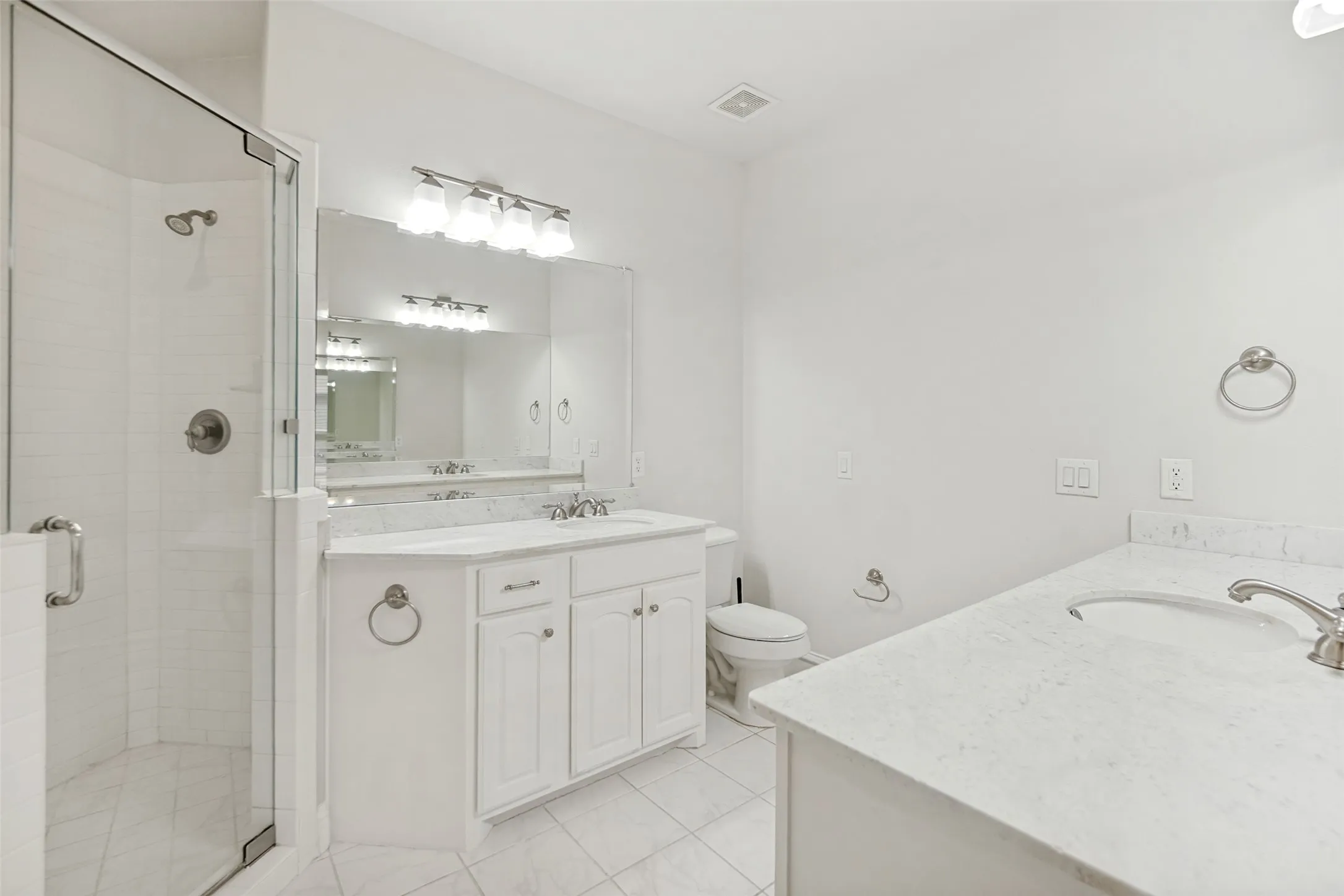 Dual vanity with undermount sinks, frameless glass shower enclosure, white cabinetry, and light-toned countertops