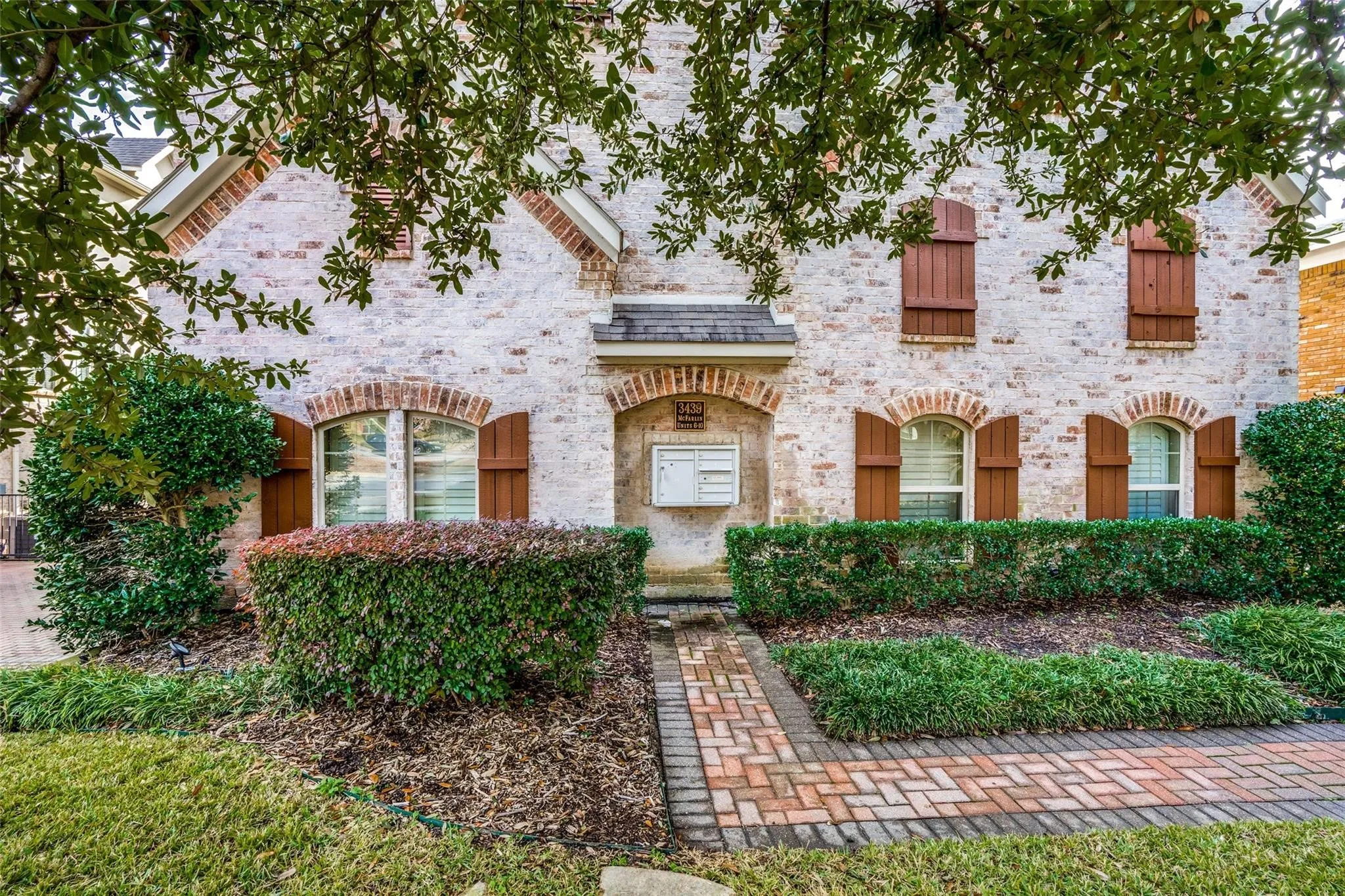 Brick exterior with arched window detailing, wood shutters, and a herringbone brick pathway