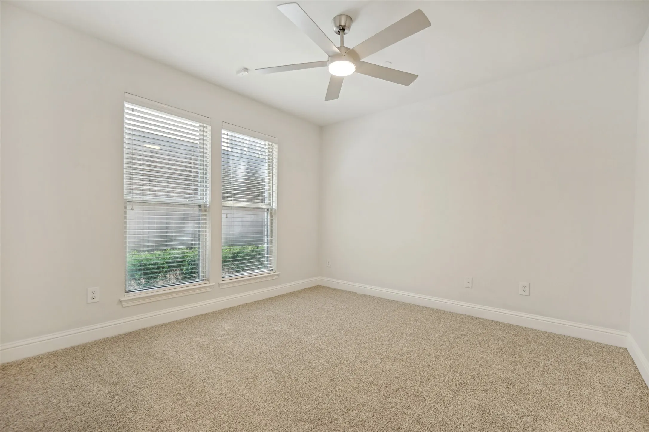 Neutral-toned carpet flooring, two windows with blinds, and a ceiling fan with integrated lighting
