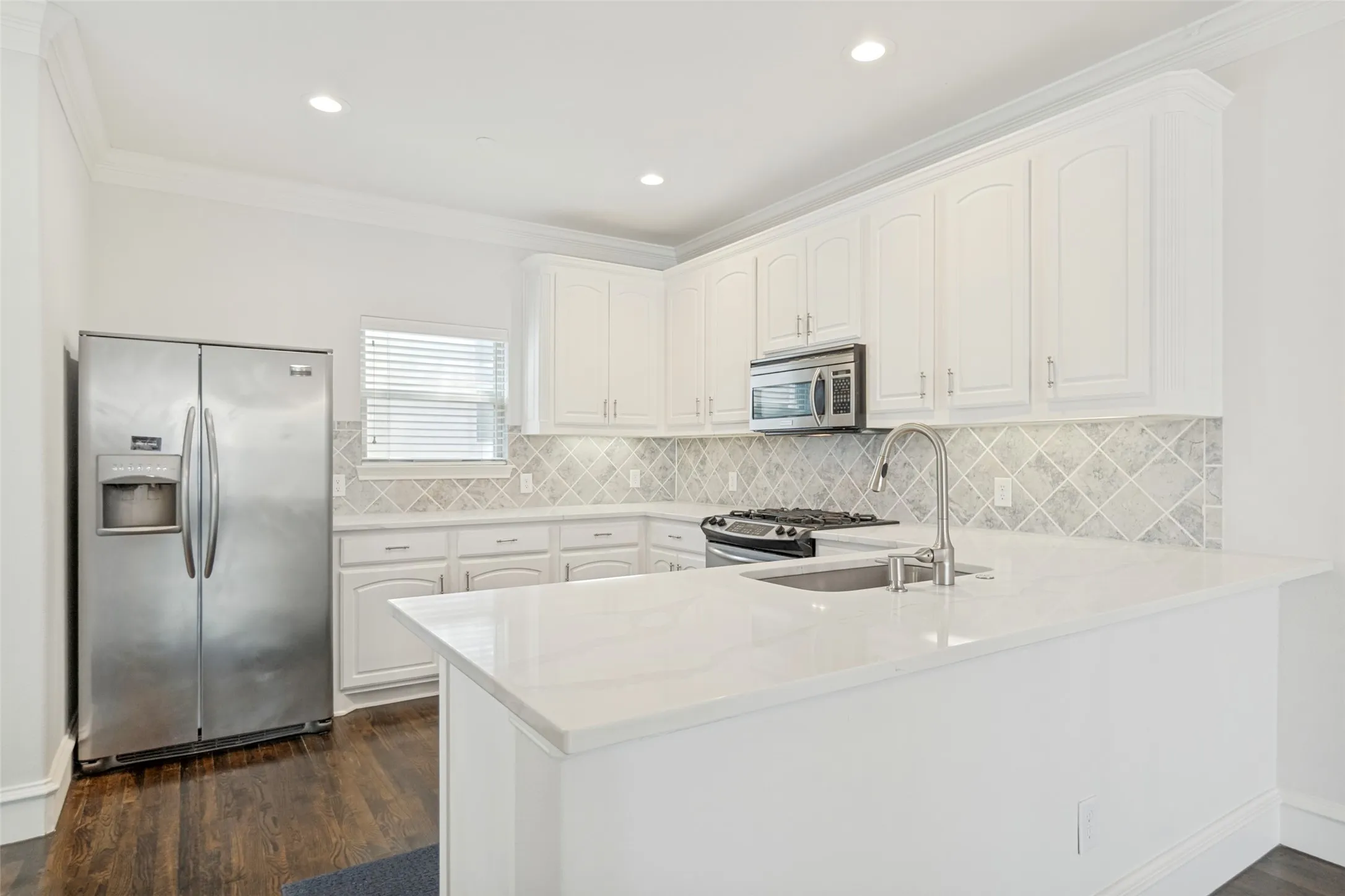 U-shaped kitchen featuring white cabinetry, stainless steel appliances, a tile backsplash, light-colored countertops, and wood-finish flooring
