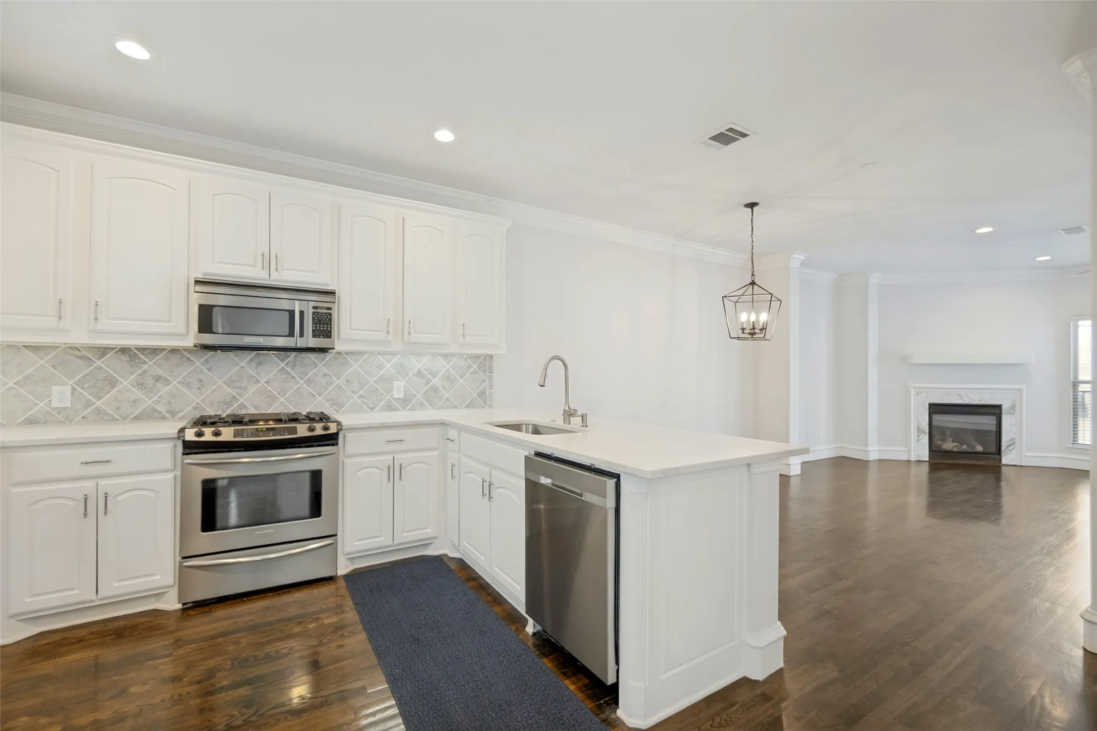 Open-concept kitchen featuring white cabinetry, stainless steel appliances, a center island, and wood-finish flooring