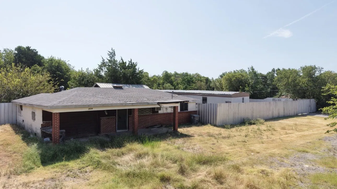 Brick façade with an integrated covered porch, a shingle roof, and a privacy fence