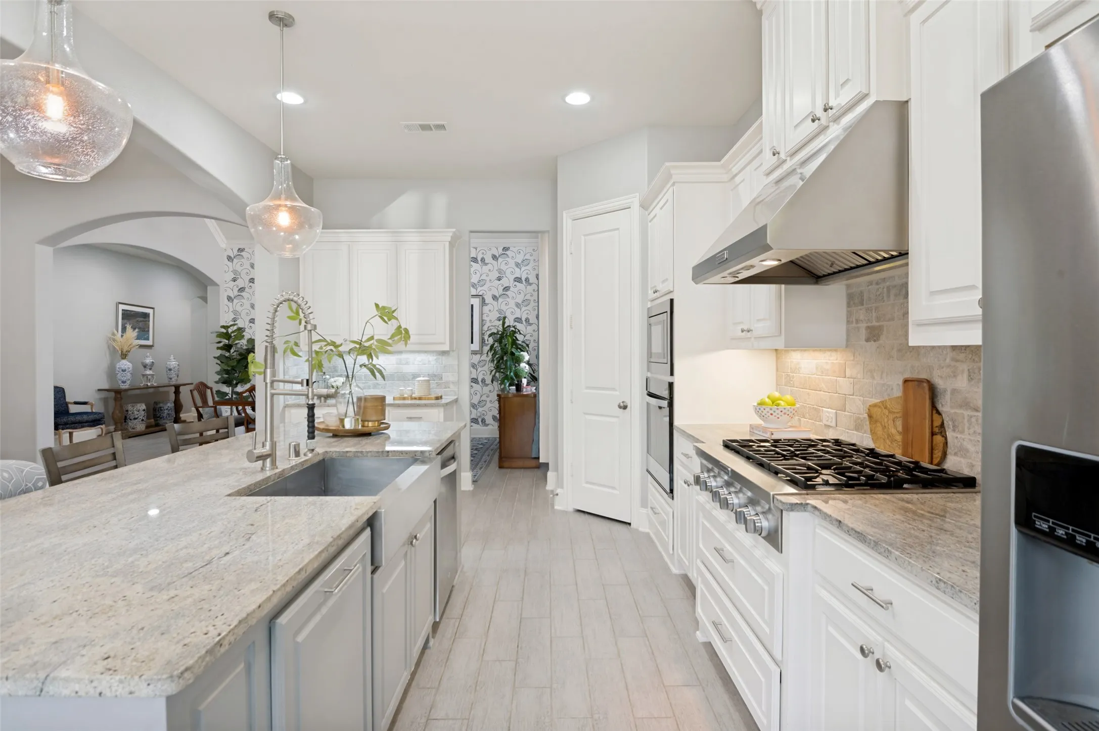 Chef's kitchen featuring a large quartz island with farmhouse sink, gas cooktop,oven, custom cabinetry, designer lighting, and a spacious walk-in pantry. Open to the dining and family room, this space is perfect for entertaining and everyday living.