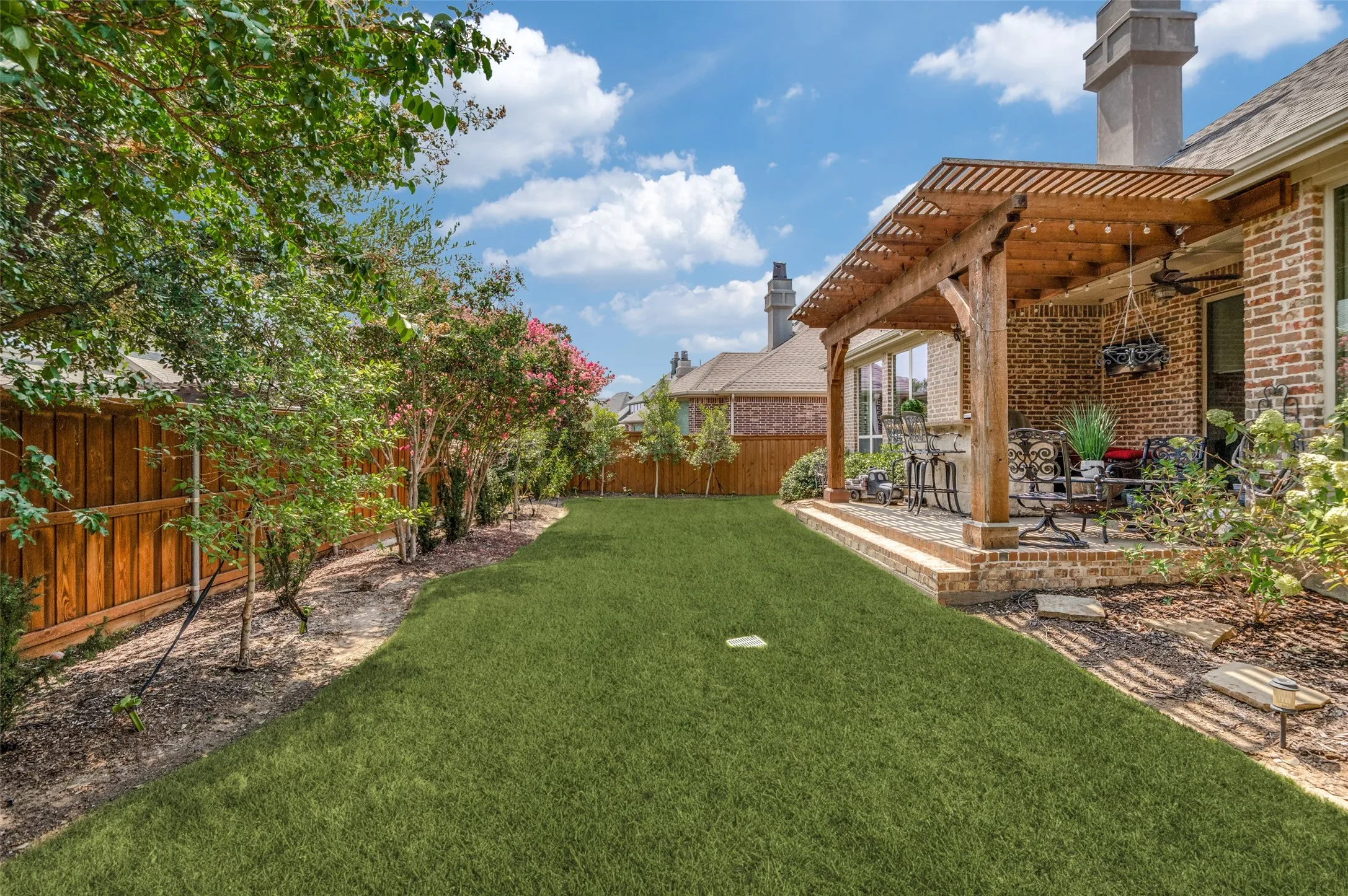 Beautifully landscaped backyard with lush green space, custom stone walkways, and a spacious covered patio with cedar pergola, creating the perfect setting for outdoor entertaining, family gatherings, or simply relaxing in your own private retreat.