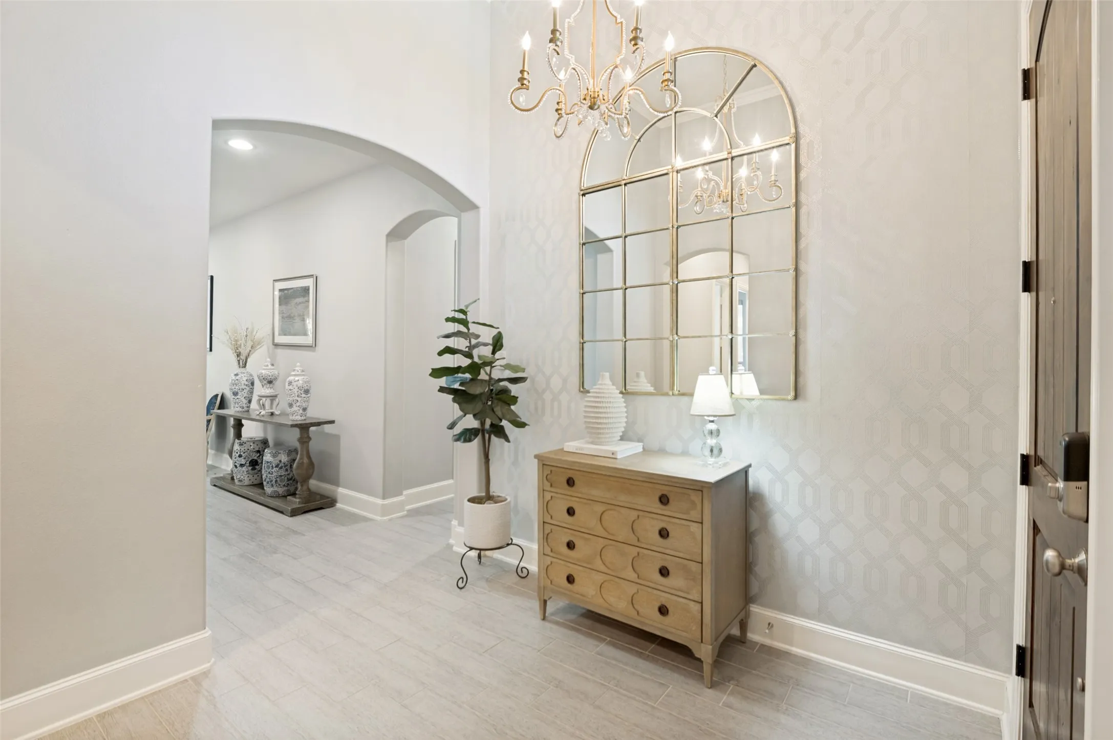 Step into luxury through an inviting foyer featuring soaring ceilings, designer lighting, elegant accent wallpaper, and beautiful wood-look tile flooring. This stunning entry sets the tone for the home's open-concept design, offering a warm welcome and a glimpse of the upscale finishes found throughout.