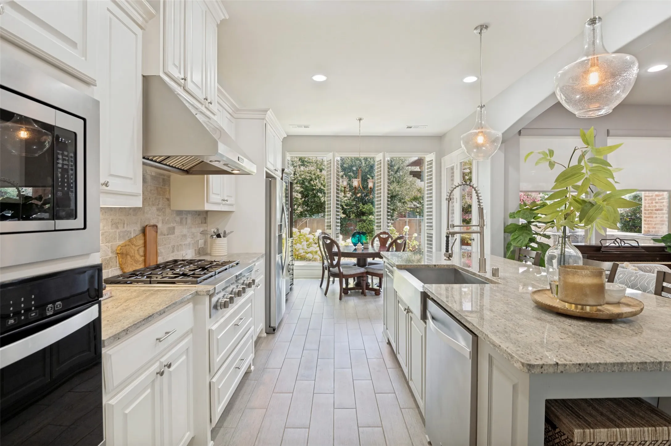 Beautiful chef's kitchen featuring a large quartz island, abundant cabinetry, and designer finishes. The adjoining breakfast room is surrounded by oversized windows with plantation shutters, filling the space with natural light and offering beautiful views of the landscaped backyard—perfect for casual dining or your morning coffee.