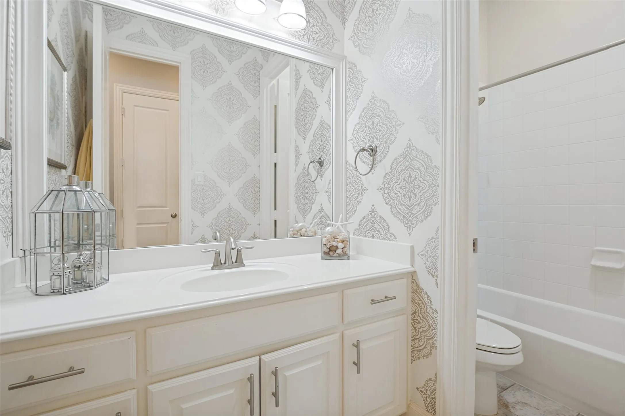 Beautifully appointed secondary bath featuring designer wallpaper, a spacious vanity with ample storage, and a tub/shower combination—perfect for family and guests.