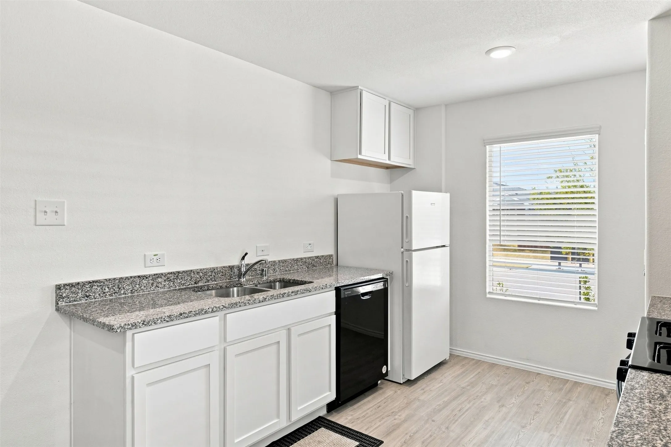 Kitchen featuring white cabinetry, speckled countertops, double basin sink, and wood-finish flooring