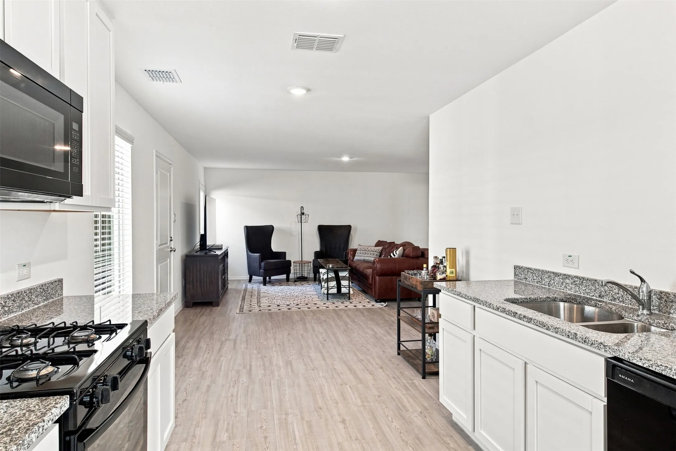 Kitchen featuring white cabinetry, granite countertops, a stainless steel sink, and a black built-in microwave