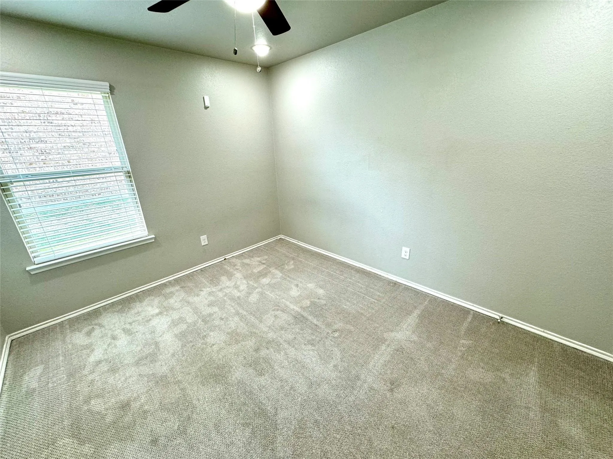 Neutral tone wall paint, light-colored carpeting, window with blinds, and a ceiling fan with integrated lighting