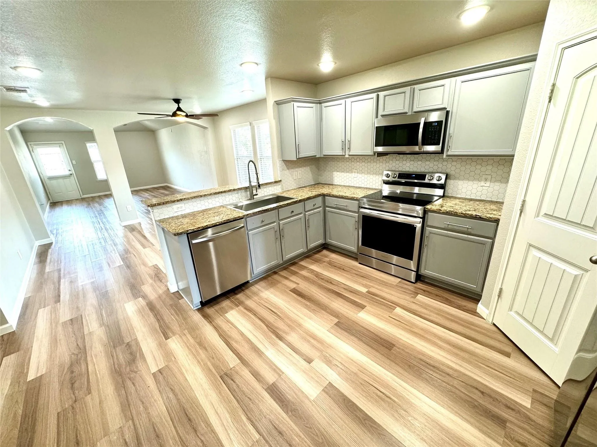 Kitchen featuring wood-finish flooring, stainless steel appliances, light gray cabinetry, and a textured backsplash