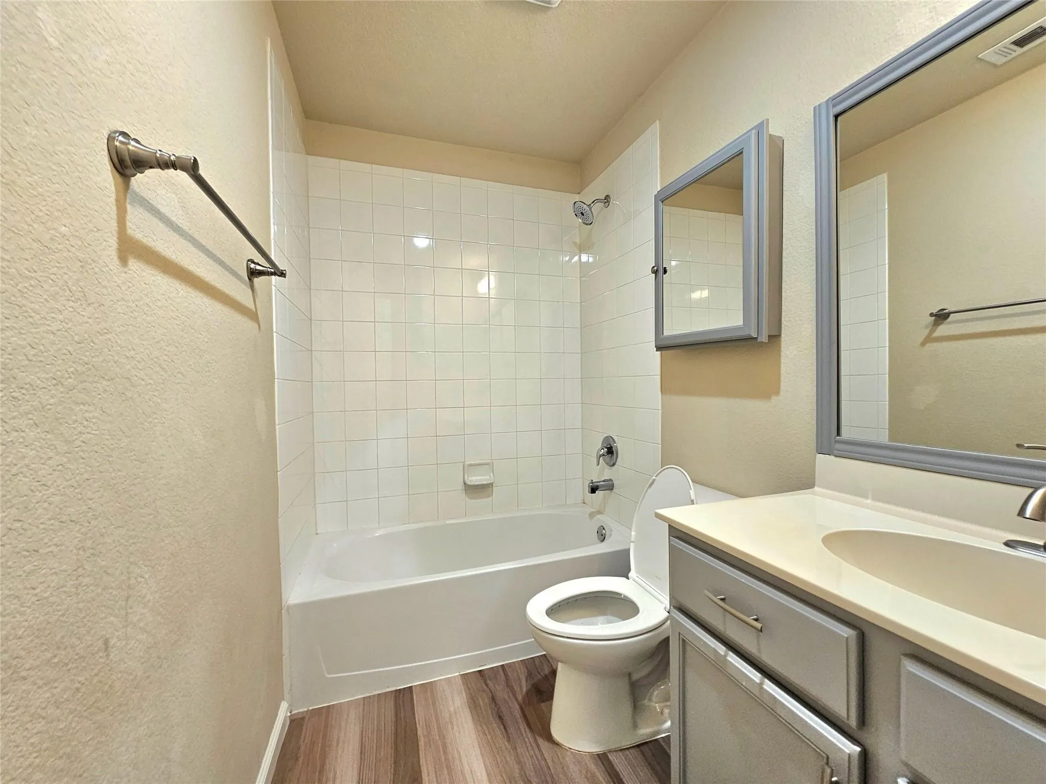 White subway-tiled shower surround with tub, gray-framed mirror, wood-finish flooring, and a vanity with a light-colored countertop