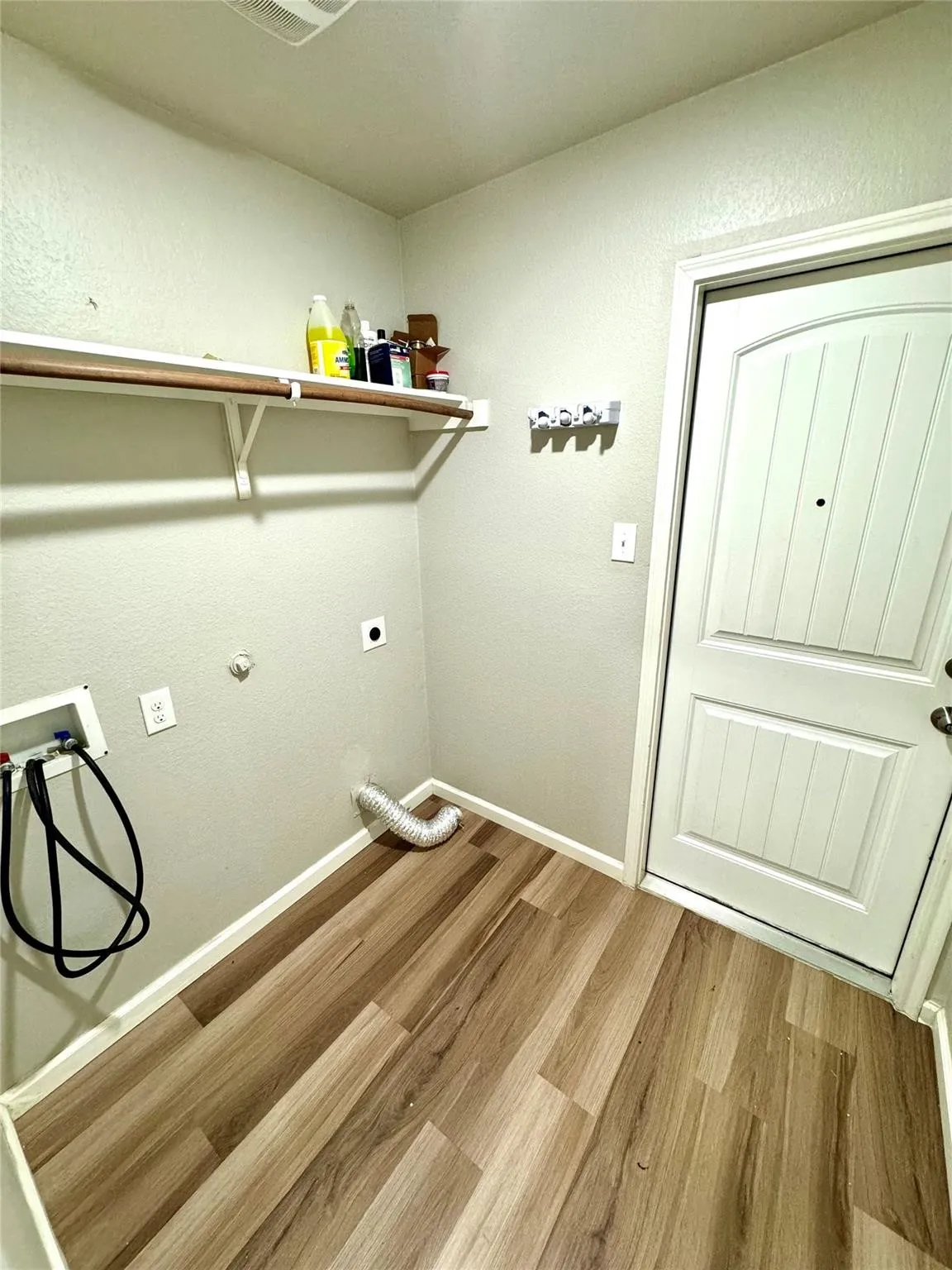 Dedicated laundry area featuring wood-finish flooring, a wall-mounted shelving unit, and a paneled door