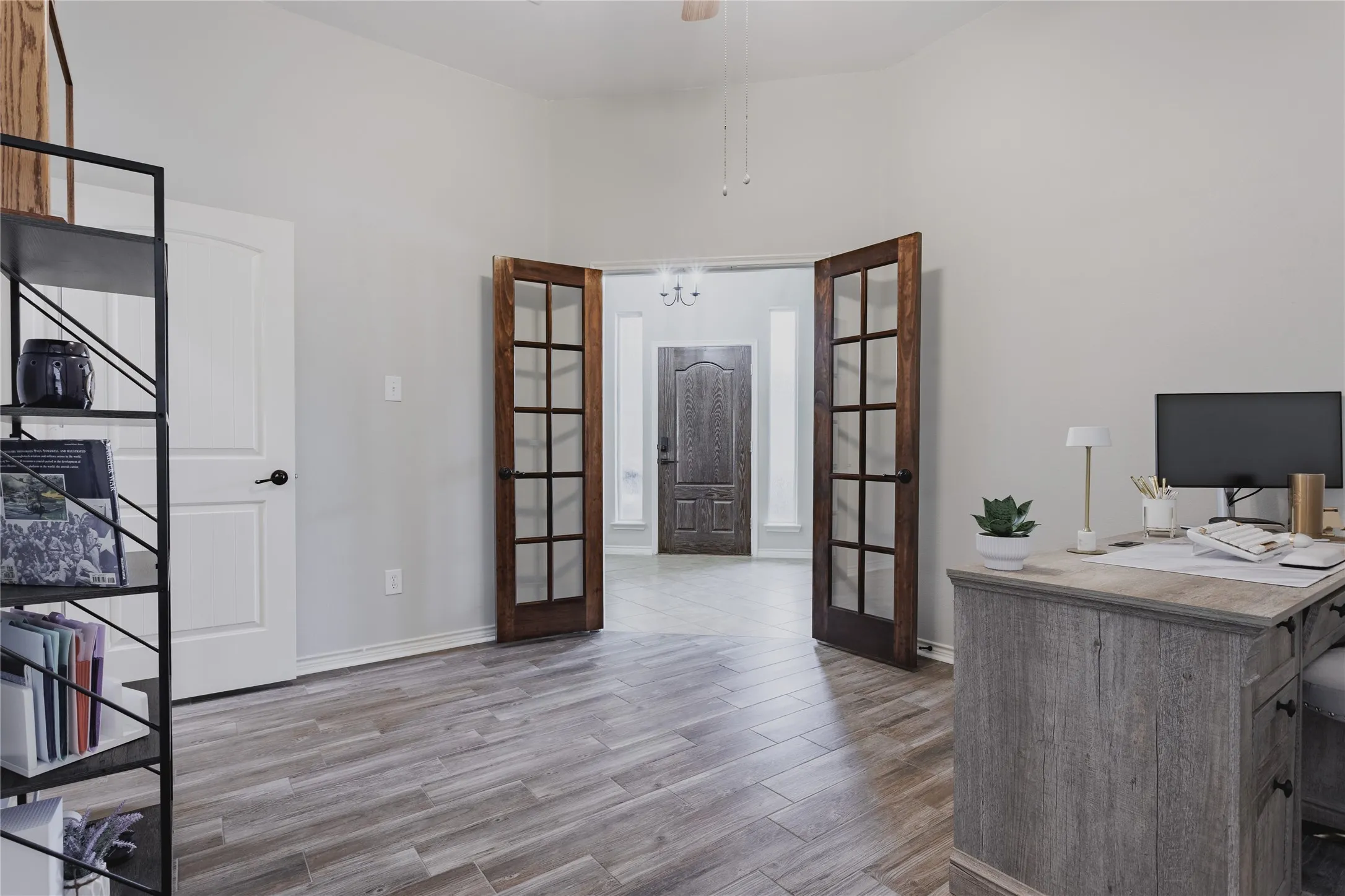 Spacious open-concept office featuring wood-finish flooring, built-in desk cabinetry with ample countertop workspace, and French doors with multiple glass panes opening to additional interior spaces