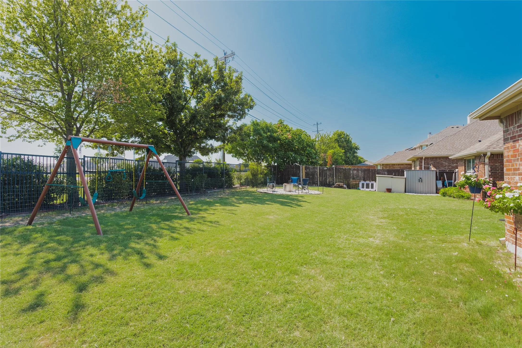 Expansive green lawn, brick exterior, dark metal fencing, mature trees, and storage sheds