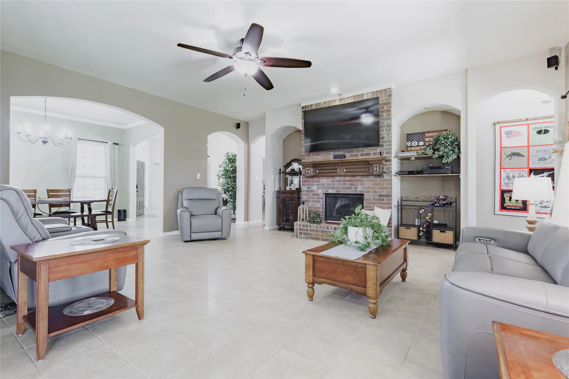 Spacious living area featuring light-toned tile flooring, a brick-surround fireplace with a wood mantle, and arched doorways