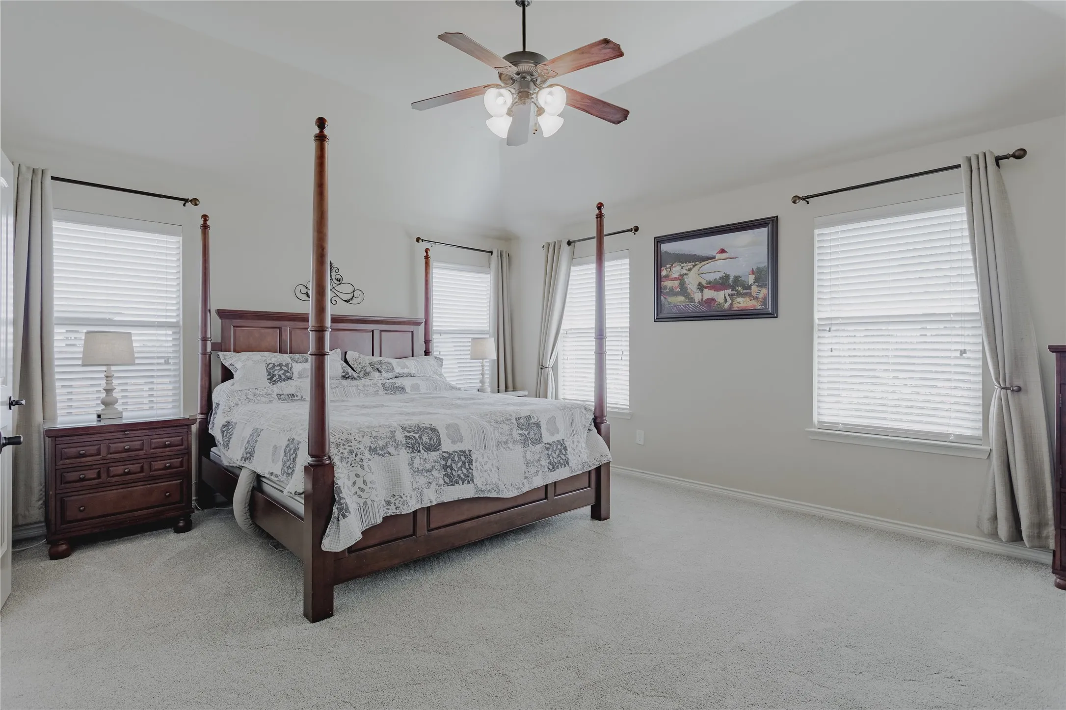 Vaulted ceiling with a ceiling fan, carpeted flooring, multiple windows with blinds, and neutral wall tones