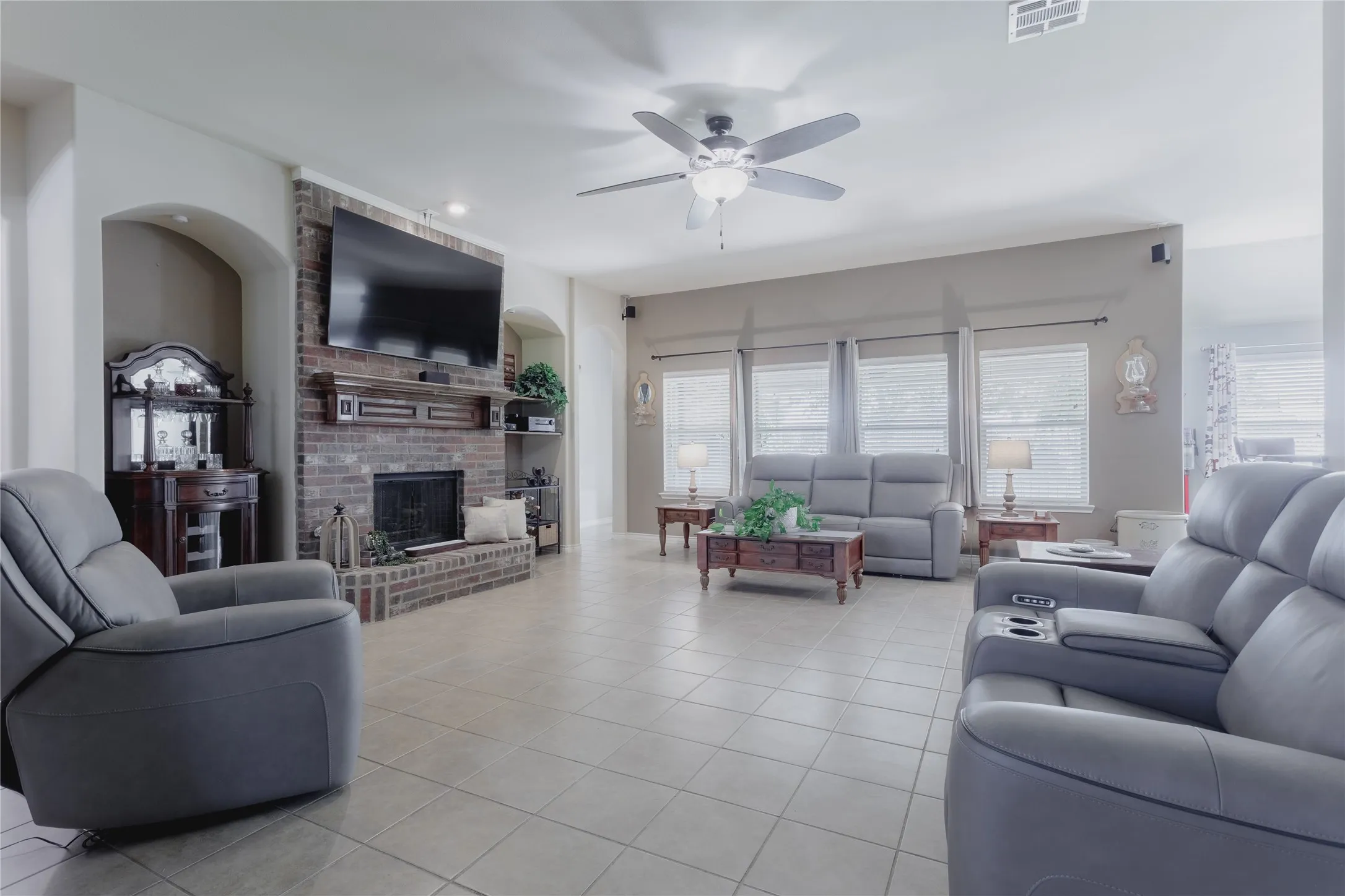 Spacious living area showcasing neutral tile flooring, dual gray upholstered seating, and a ceiling fan