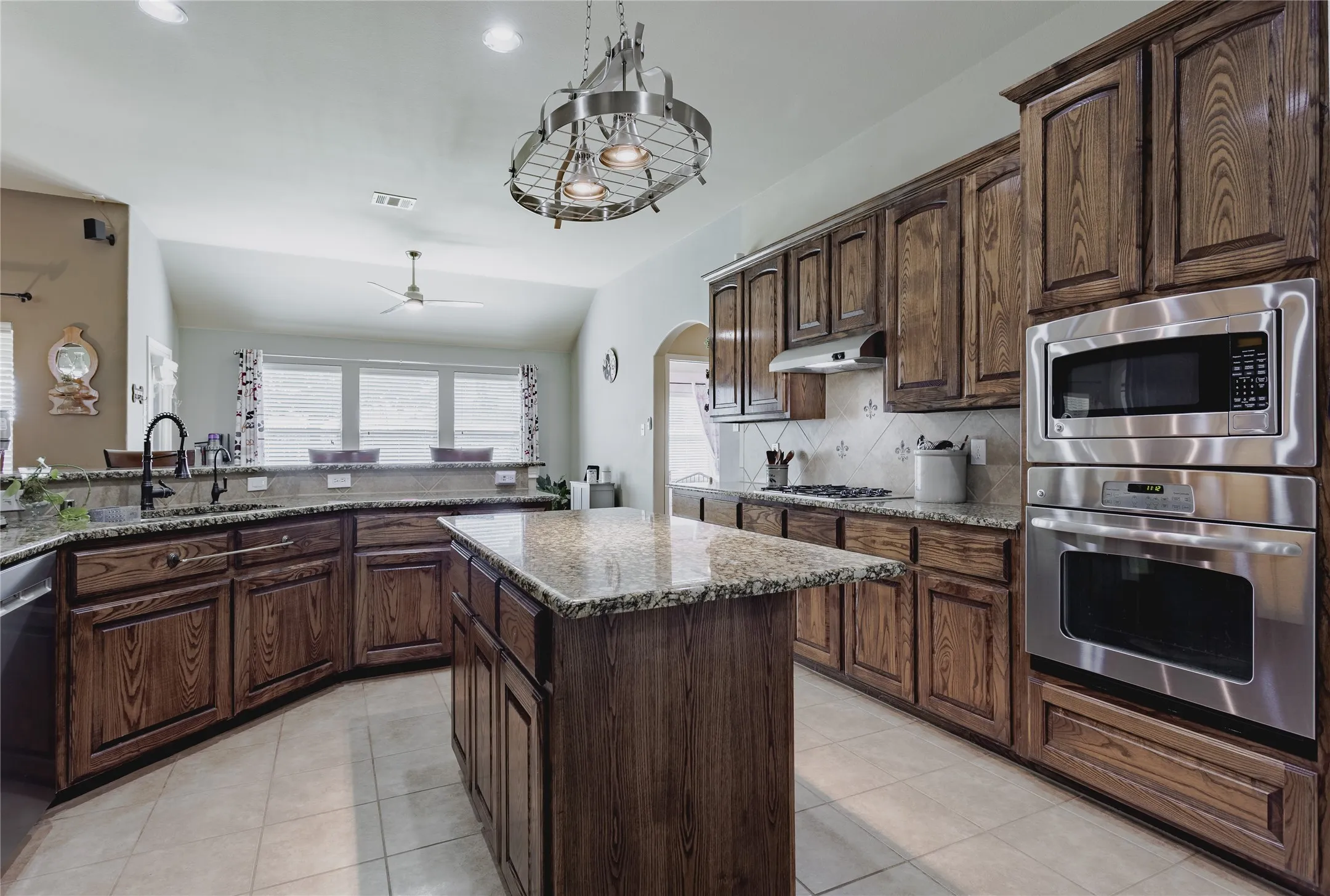 Spacious kitchen featuring wood cabinetry, granite countertops, stainless steel appliances, a center island, and tile flooring