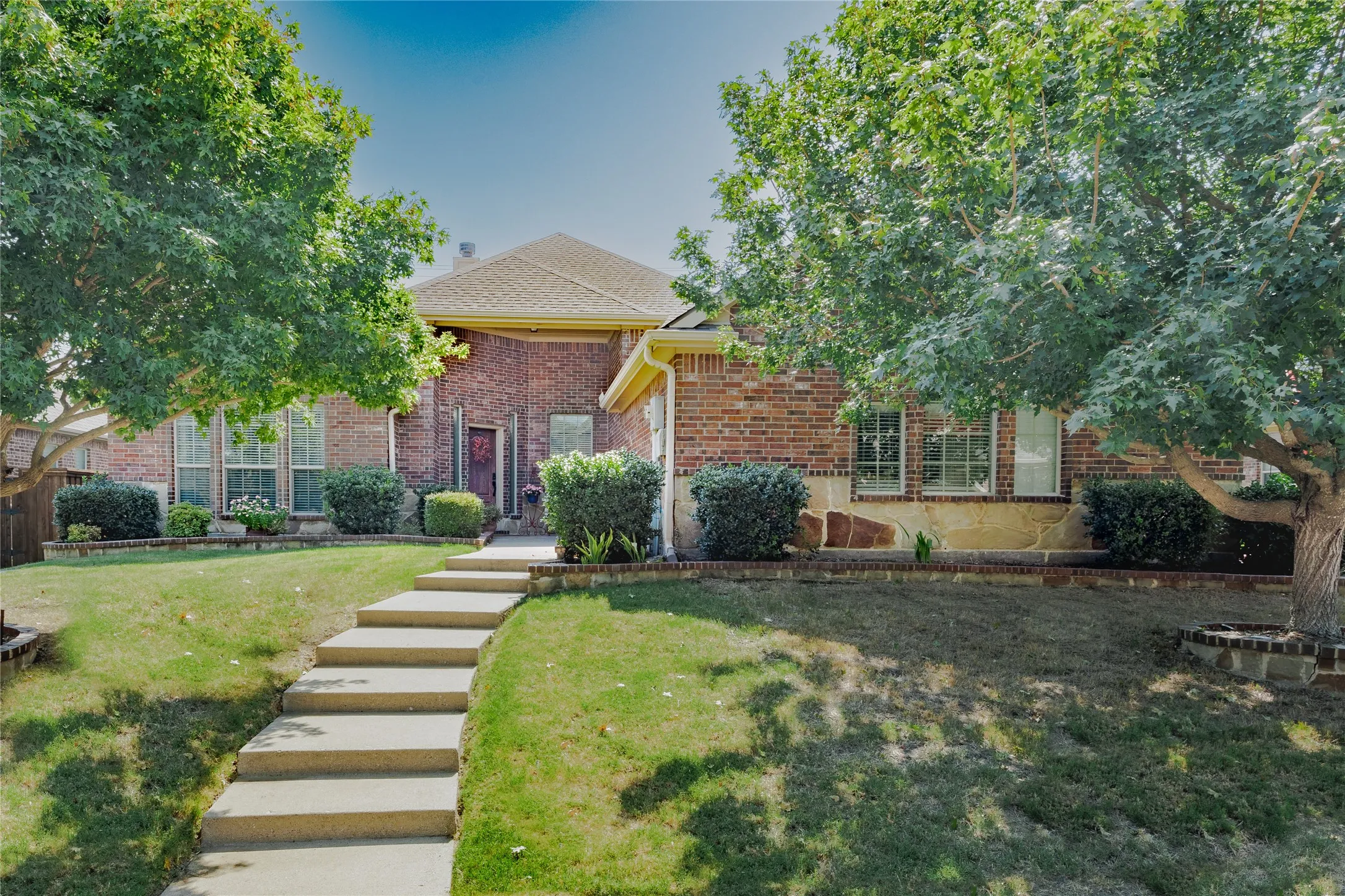 Brick exterior with a covered entry, tiered walkway, and established landscaping