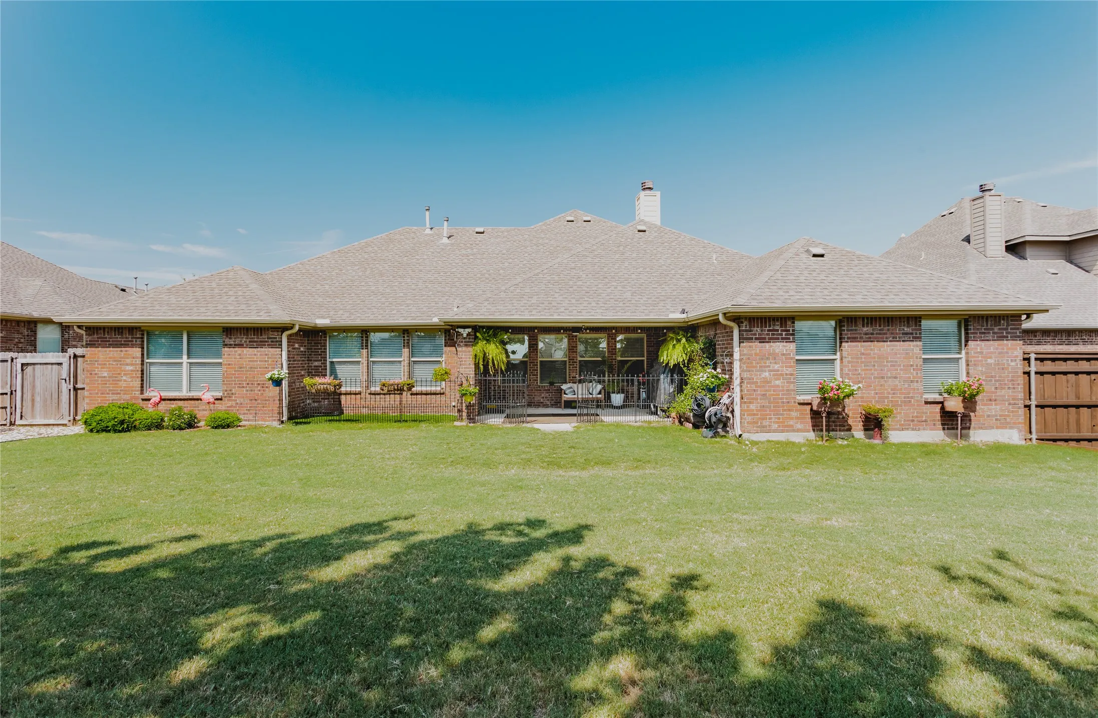 Expansive single-story brick residence with a manicured lawn, mature landscaping, and covered patio