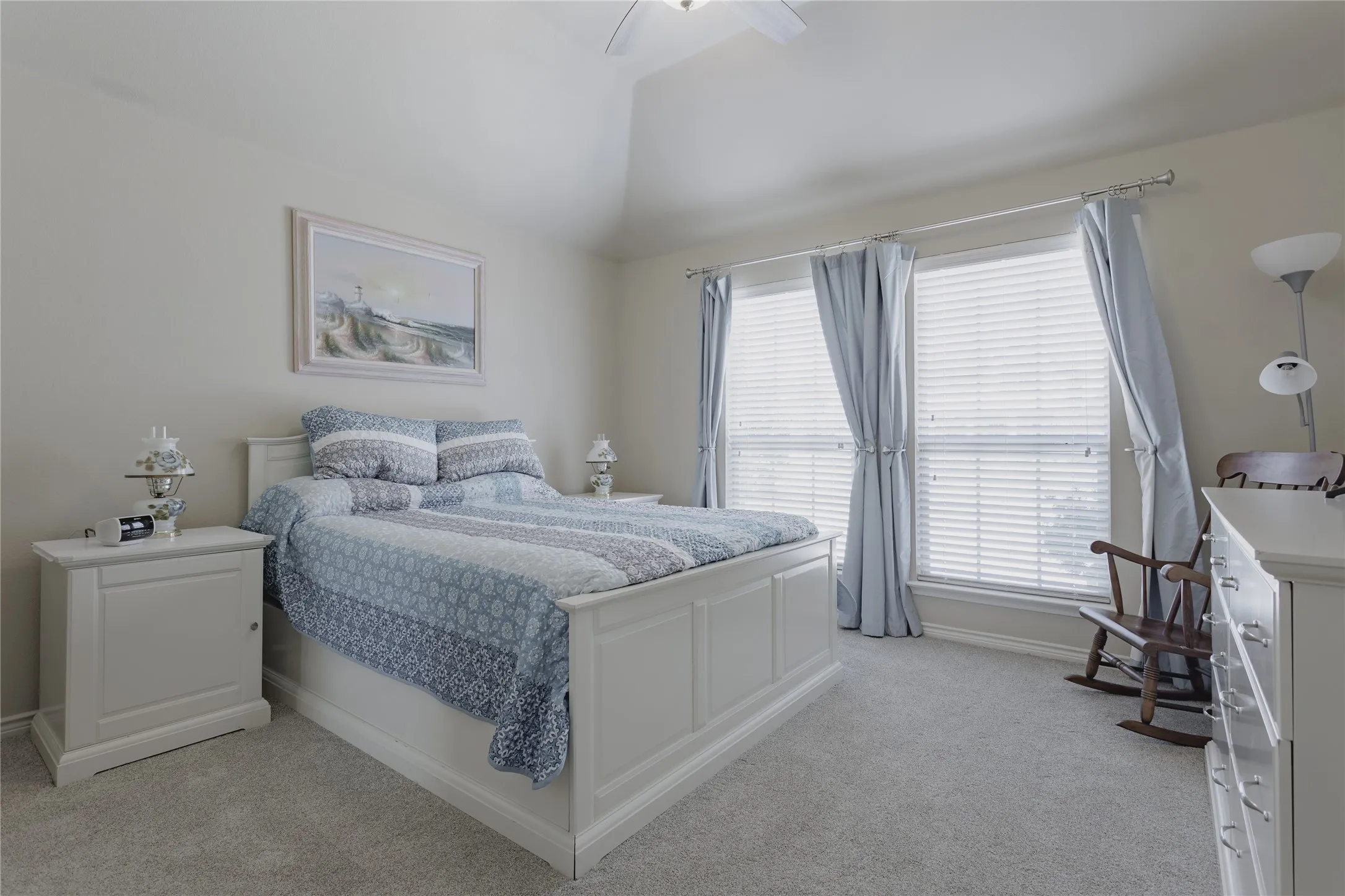 Bright bedroom featuring a white painted wood bed frame, dual nightstands with task lighting, vaulted ceiling with recessed lighting, and expansive glass doors opening to natural light