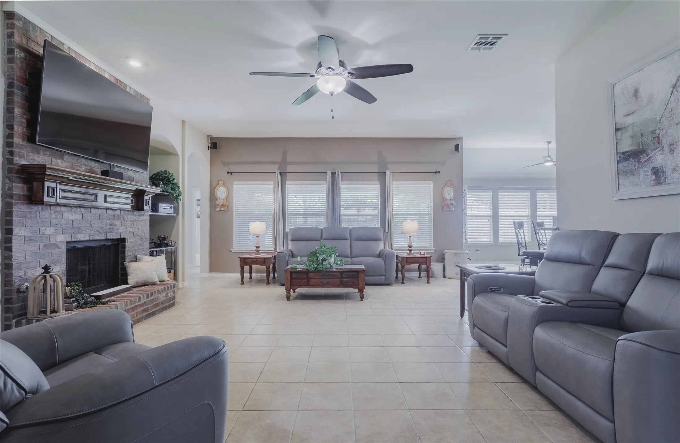 Open-concept living area featuring tile flooring, ceiling fan, and abundant natural light from multi-pane glass doors