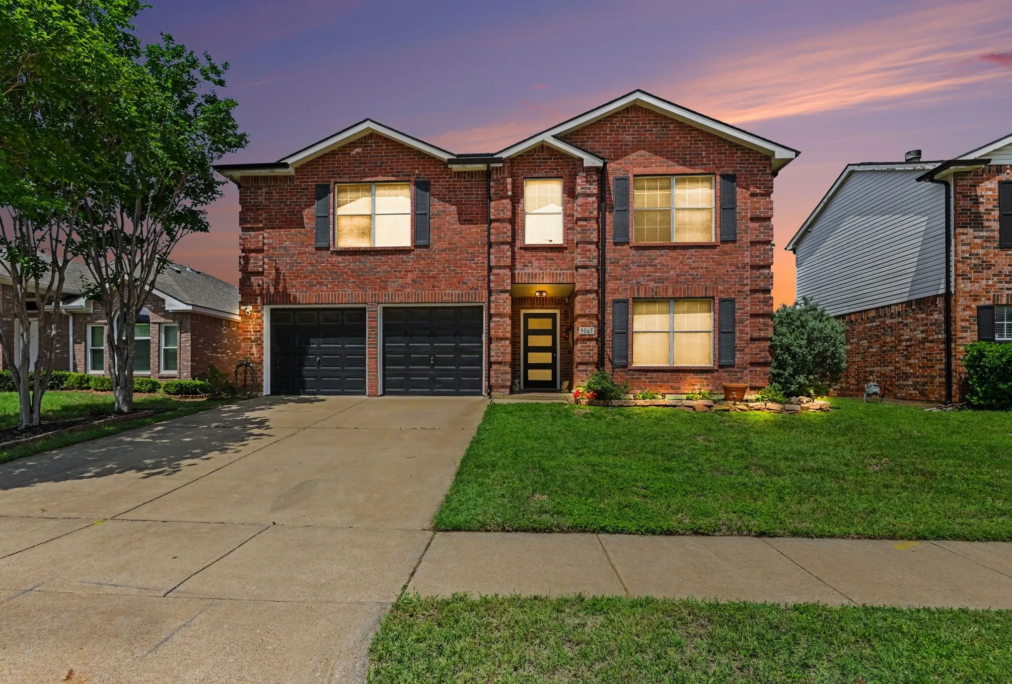 Elegant two-story brick Colonial with dual-car garage, illuminated by warm interior lighting