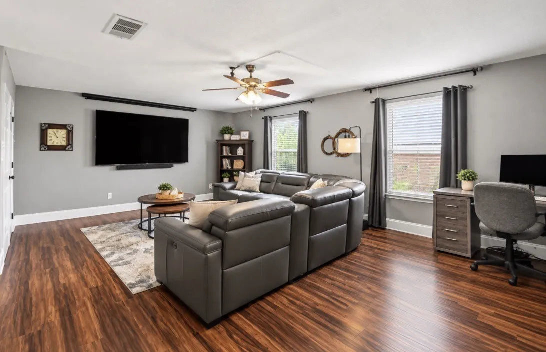 Wood-finish flooring throughout, multiple windows, ceiling fan with integrated lighting, and neutral wall paint