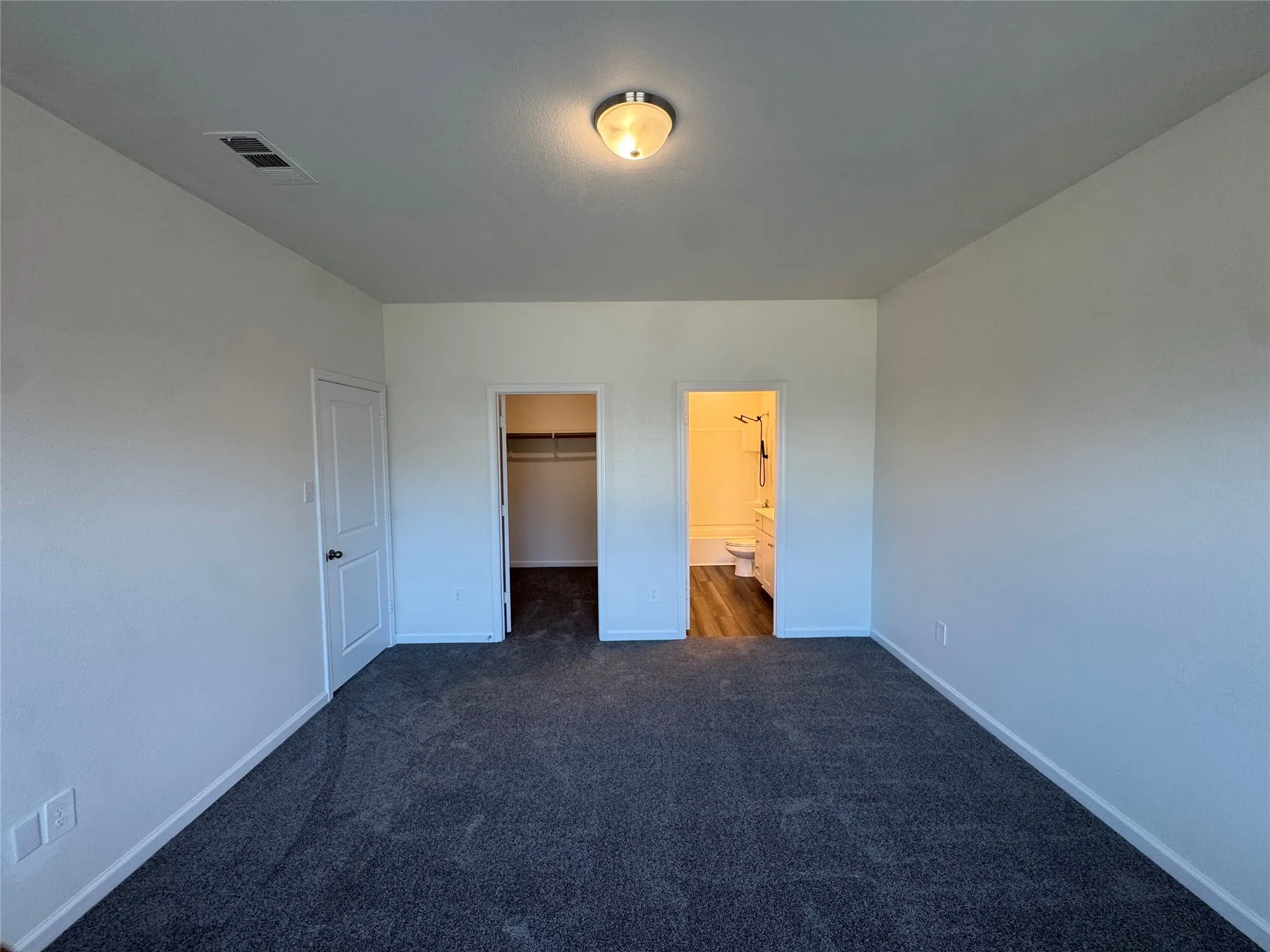 Spacious room featuring neutral carpeting, a built-in closet with shelving, and an en-suite bathroom with wood-finish flooring