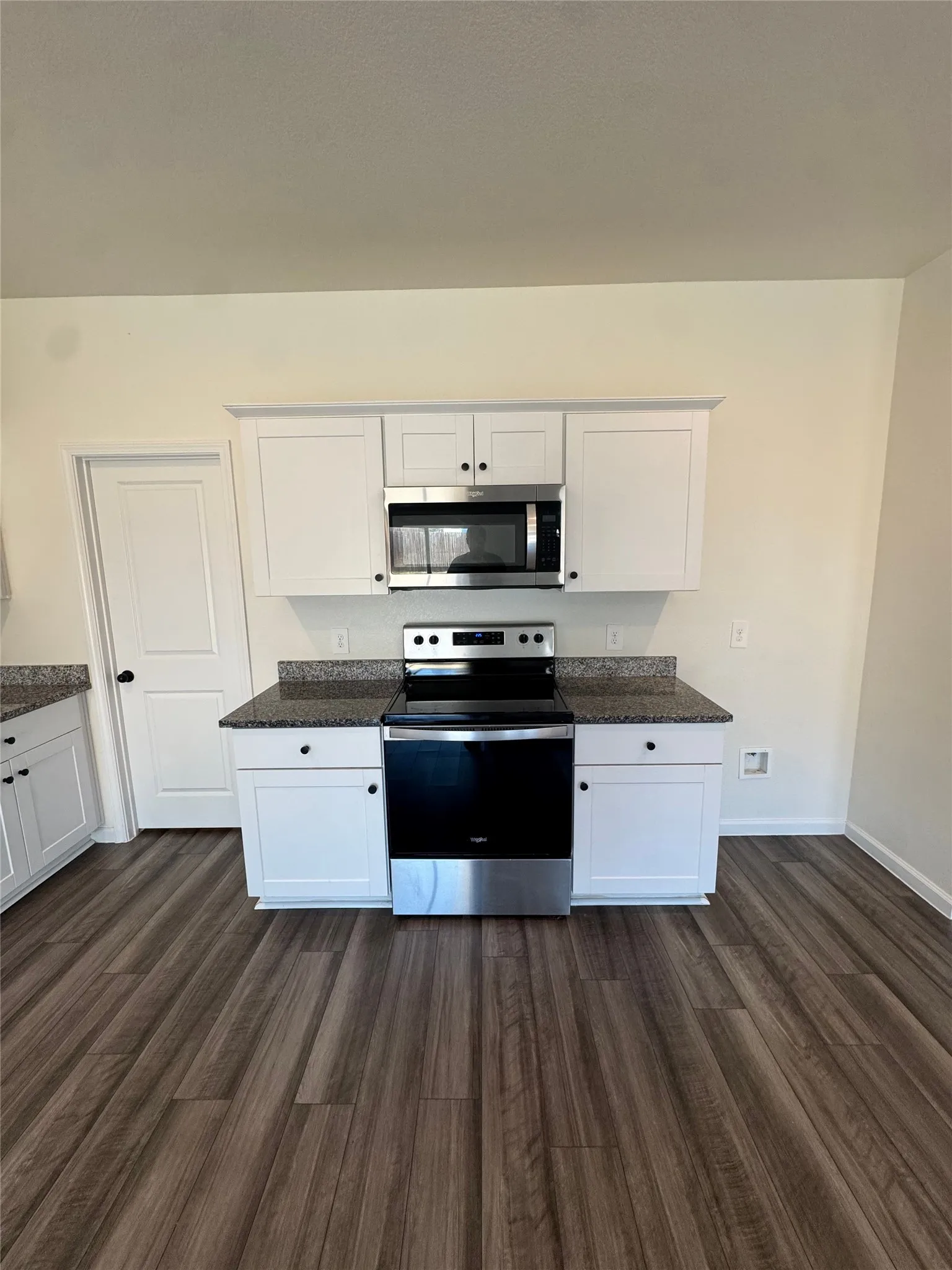 White upper and lower cabinetry, stainless steel microwave, black electric range, granite-patterned countertops, and wood-finish flooring