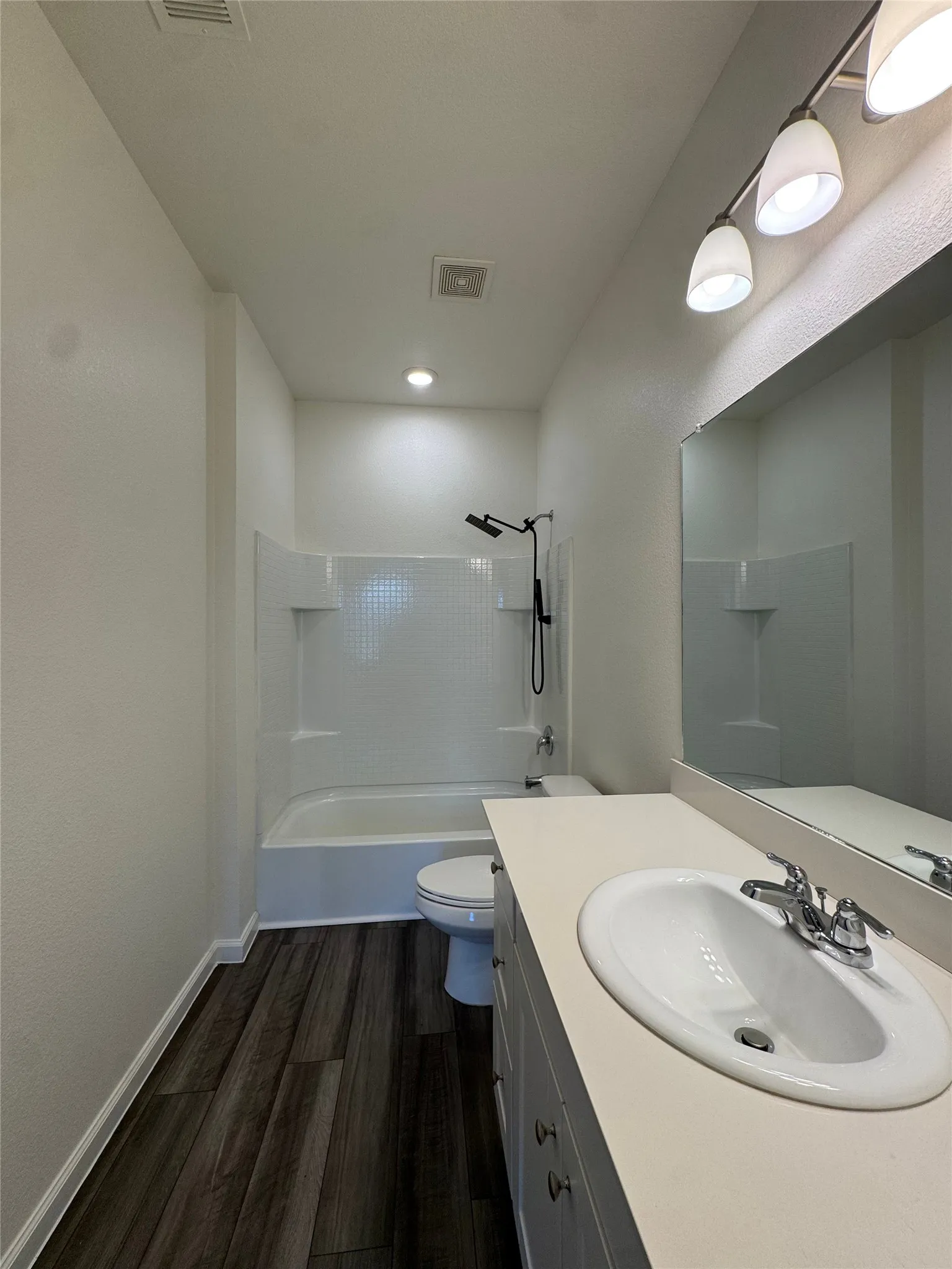 Wood-finish flooring with a white vanity featuring an integrated sink, chrome faucet, and a wall-mounted mirror