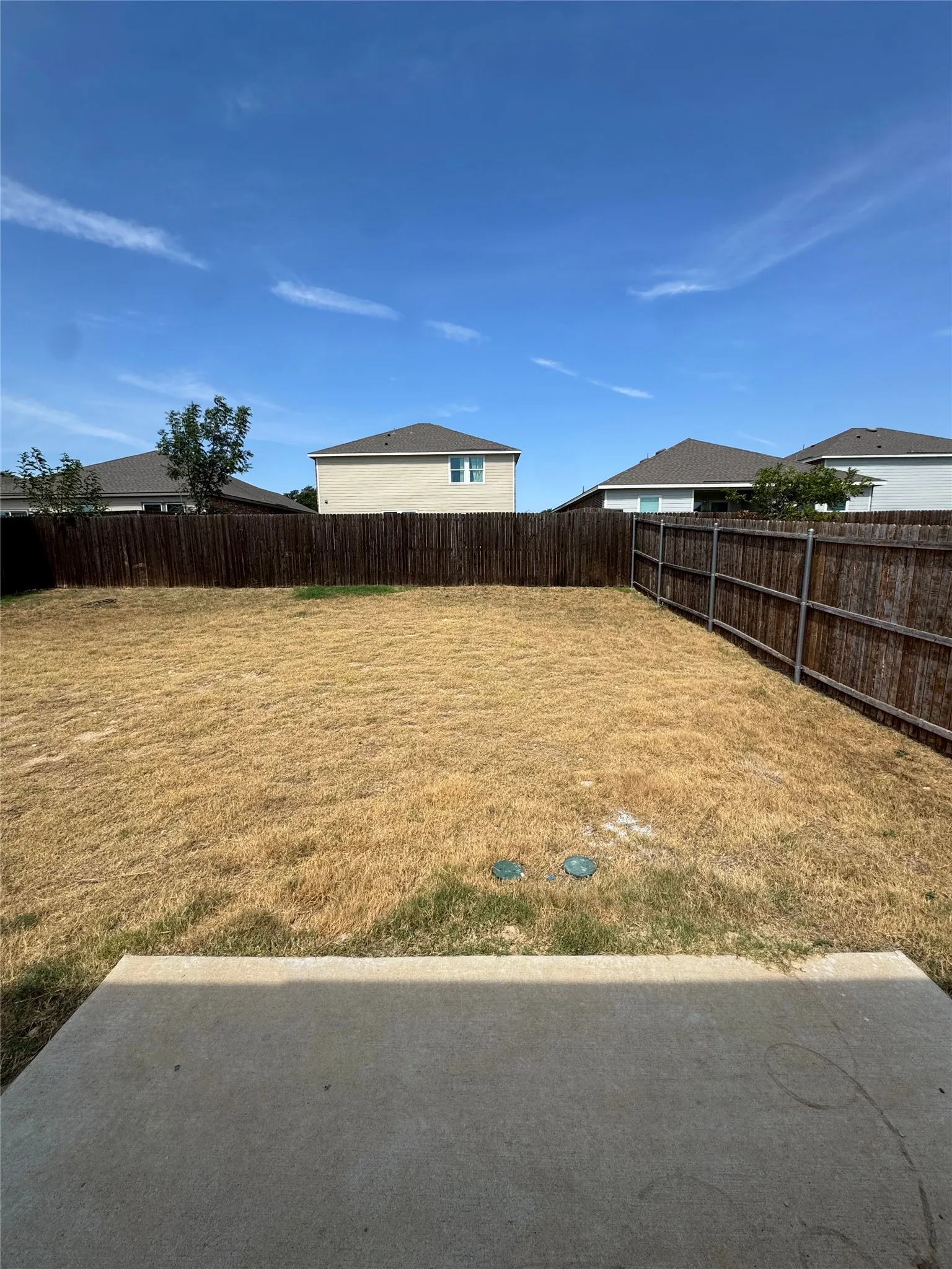 Expansive backyard featuring a concrete patio and a perimeter wood privacy fence