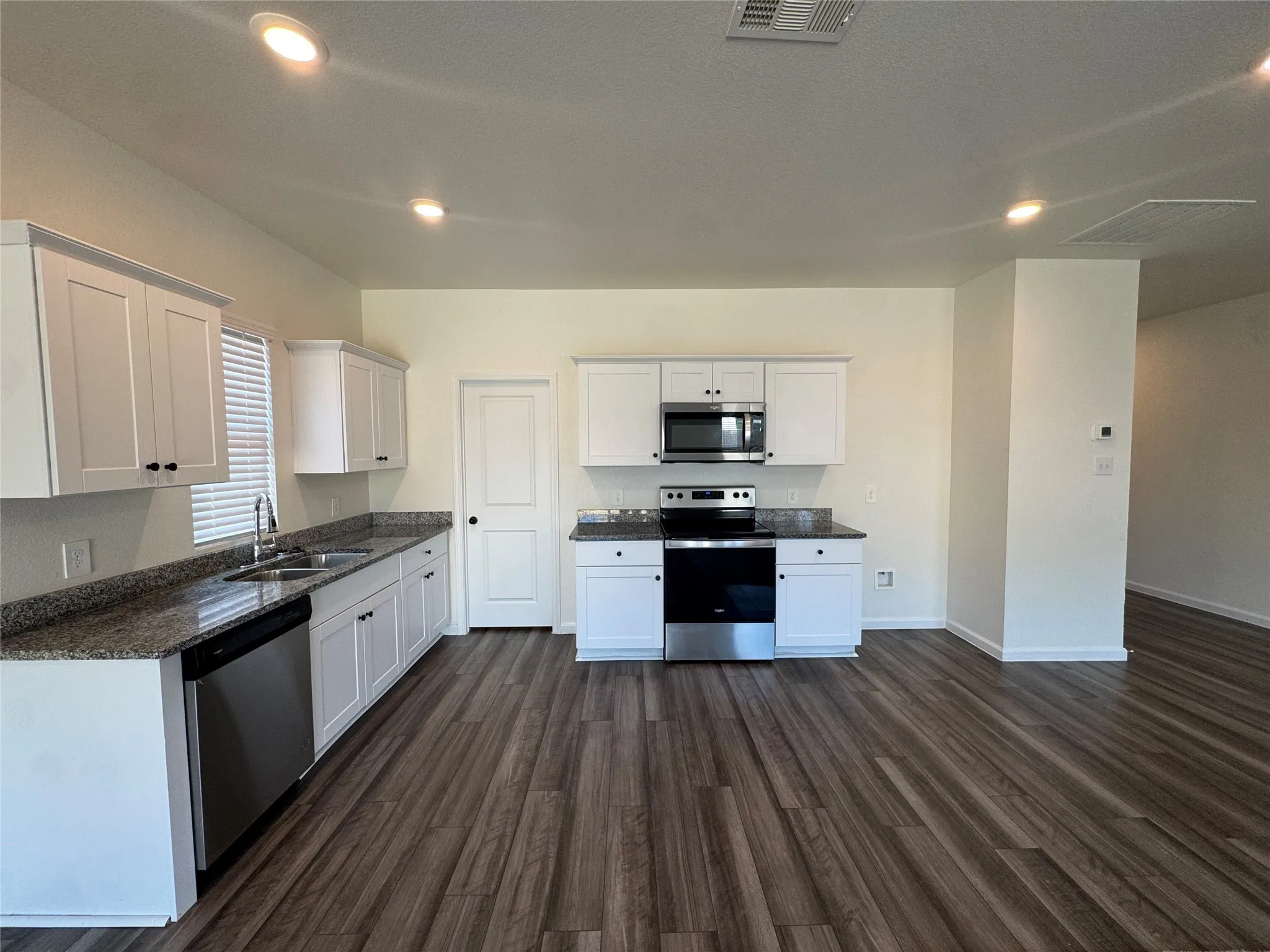 Kitchen featuring wood-finish flooring, white cabinetry, granite countertops, stainless steel appliances, and recessed lighting