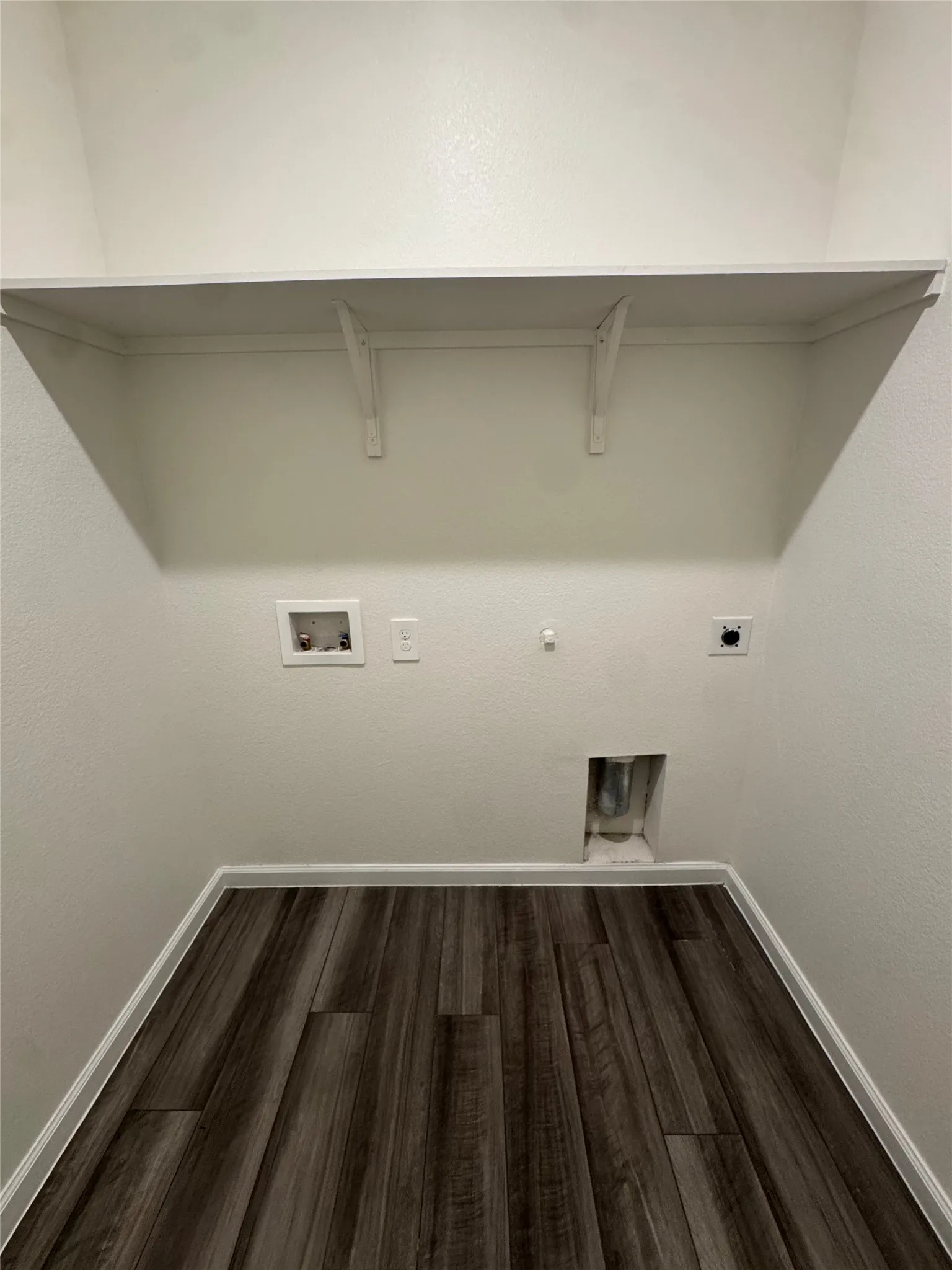 Laundry area featuring wood-finish flooring and an upper storage shelf
