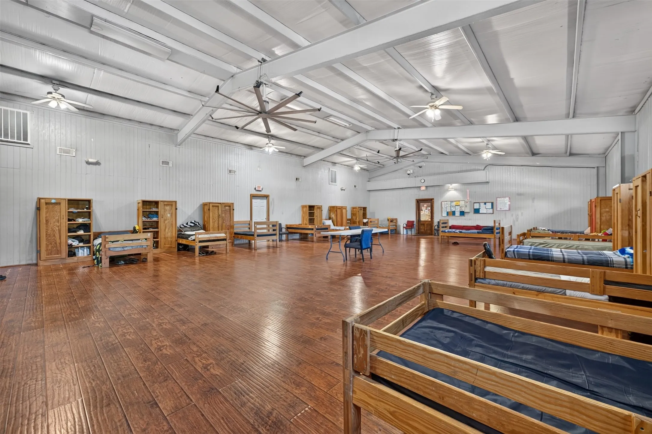 Spacious open room featuring wood-finish flooring, exposed beam ceiling, and multiple ceiling fans