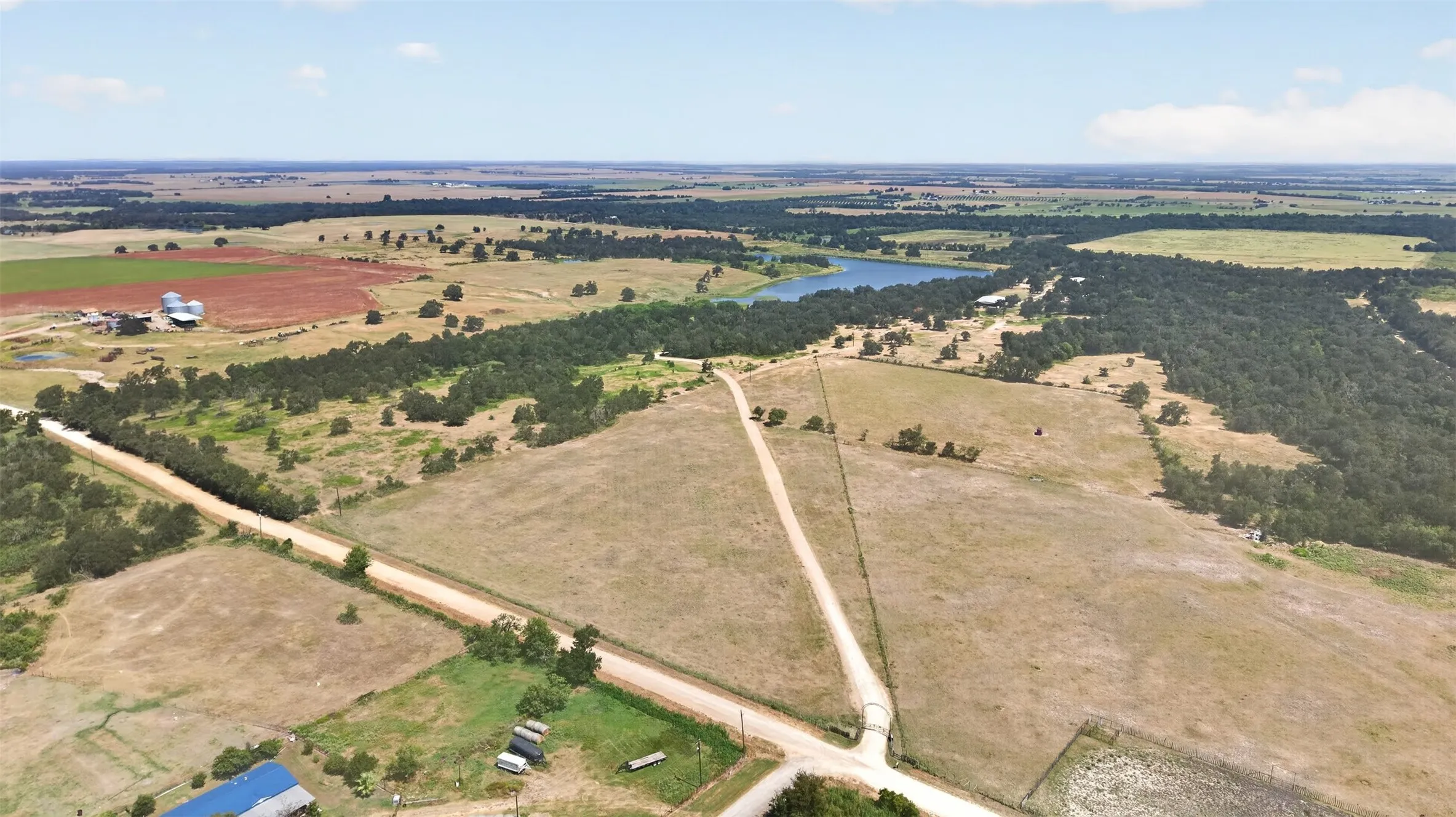 Expansive acreage with a visible water body, mature tree lines, and open fields, featuring a prominent dirt road system