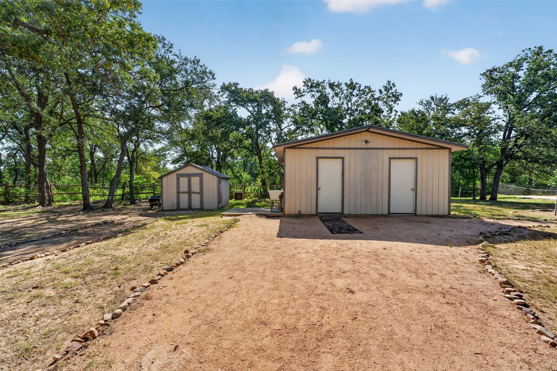 Outbuilding with two exterior doors, additional detached shed, and surrounding mature trees