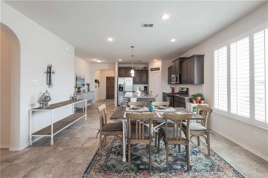 Open-concept living space with recessed lighting, tile flooring, kitchen with dark wood cabinetry, stainless steel appliances, and a central island
