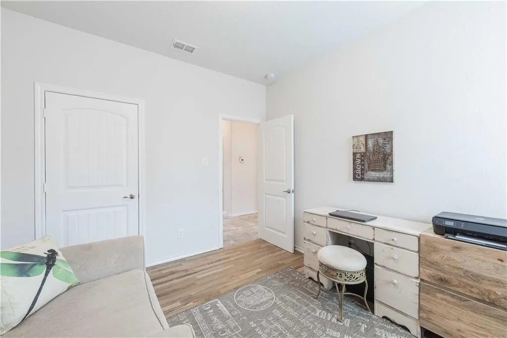 Bright home office featuring warm wood-finish flooring, white six-panel doors, built-in cabinetry with drawers and open shelving, and recessed ceiling lighting
